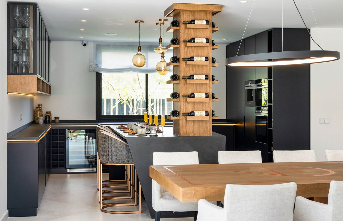 Kitchen with a breakfast bar, wine tower, and dark cabinetry. Dining table is in the foreground.