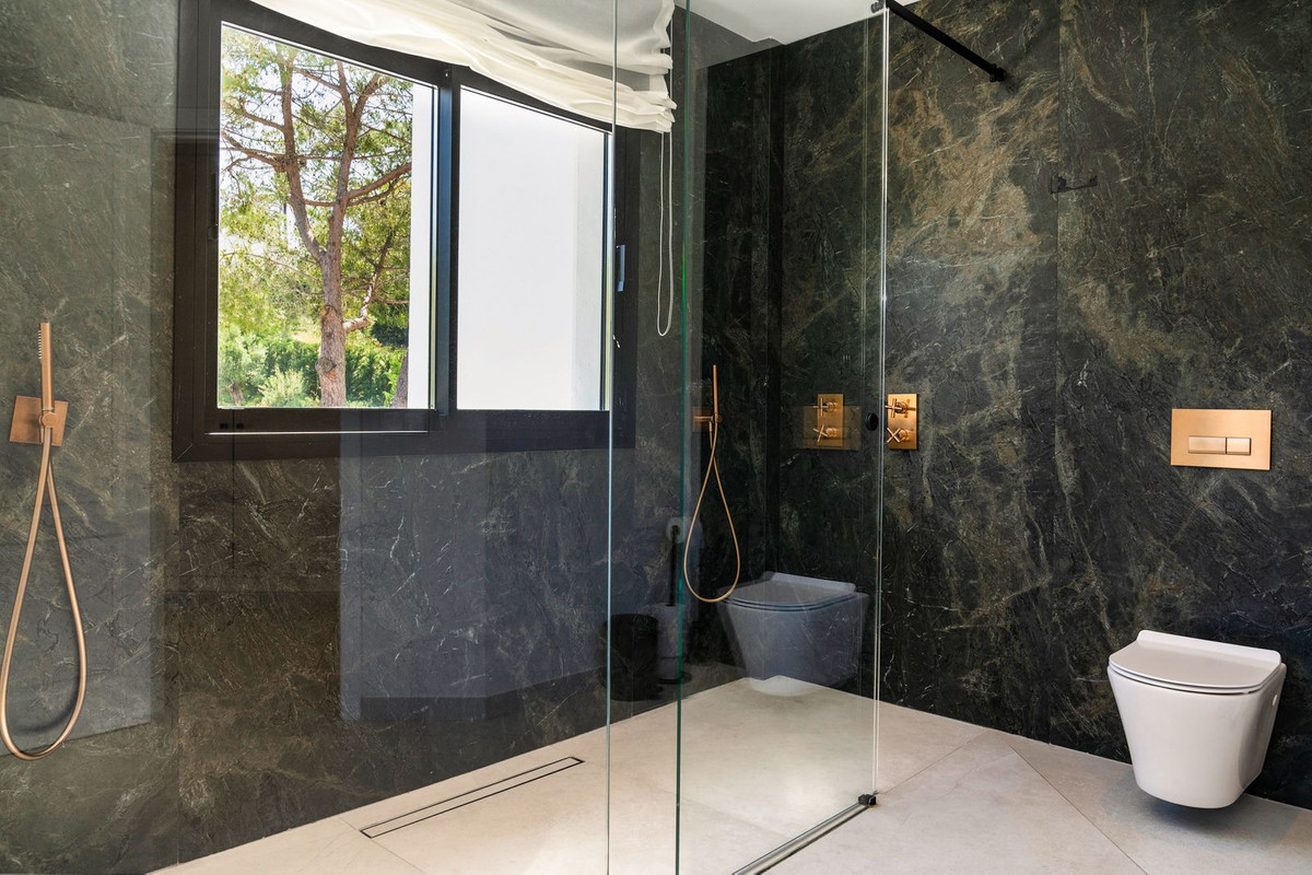 Bathroom with dark marble walls, a walk-in glass shower, wall-mounted toilet, and large window.