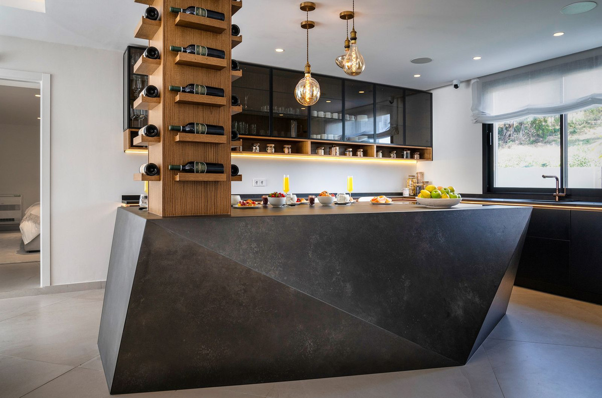Modern kitchen island with a geometric design and a central wine display tower. Fruit and snacks are on the counter.
