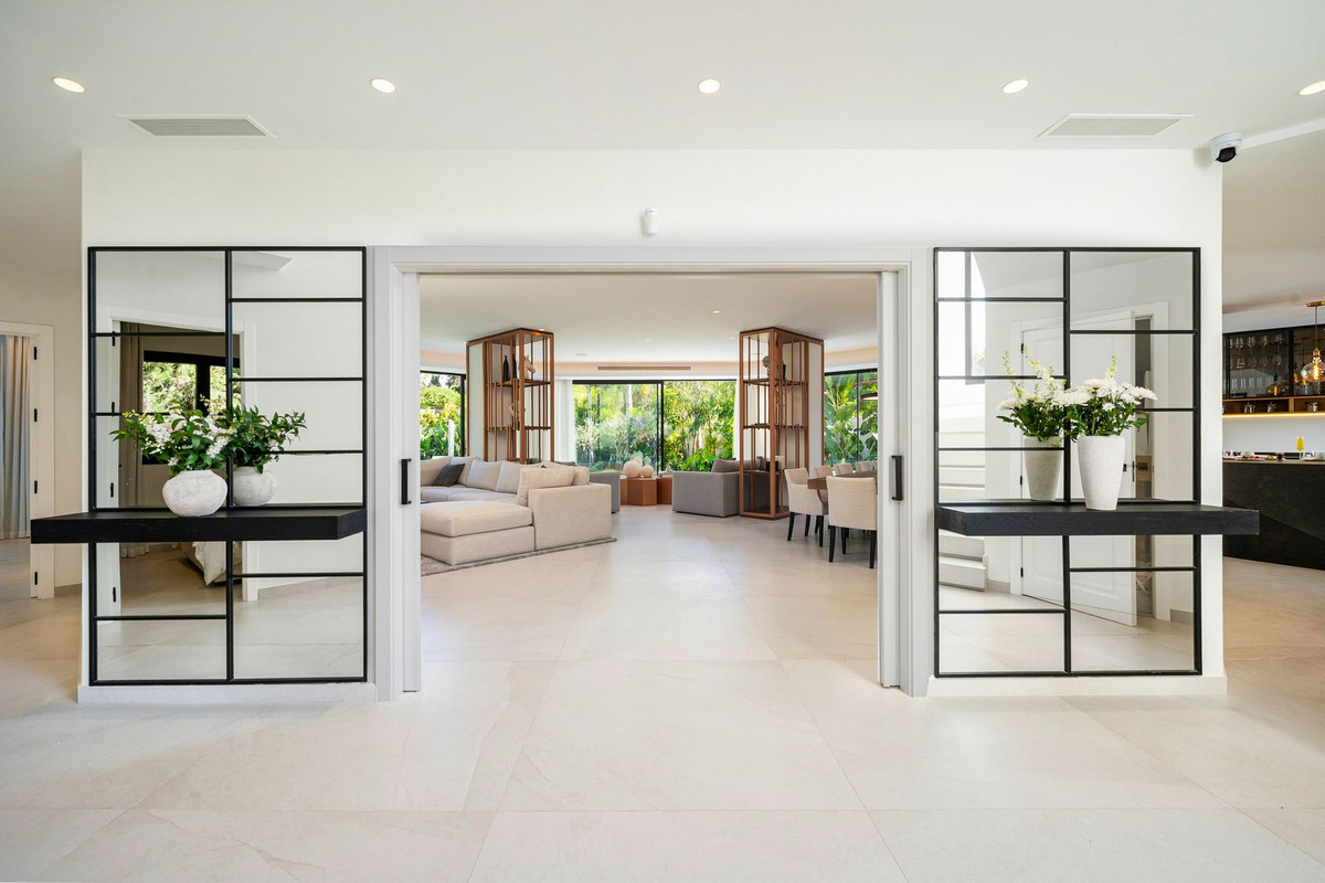 White hallway opening into a living and dining area with large windows, mirrored panels flanking the entrance.