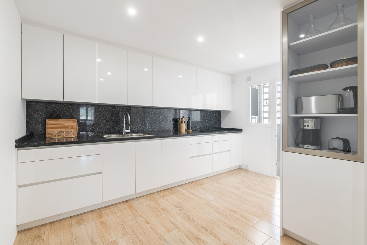 Modern kitchen featuring white cabinets, black granite backsplash, wooden floor, and appliances.