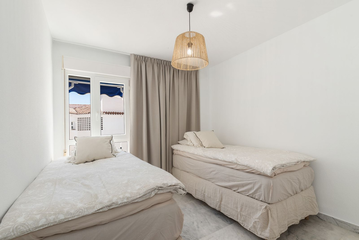 Bedroom with two single beds, a wicker pendant light, and a window with blue awnings visible outside.