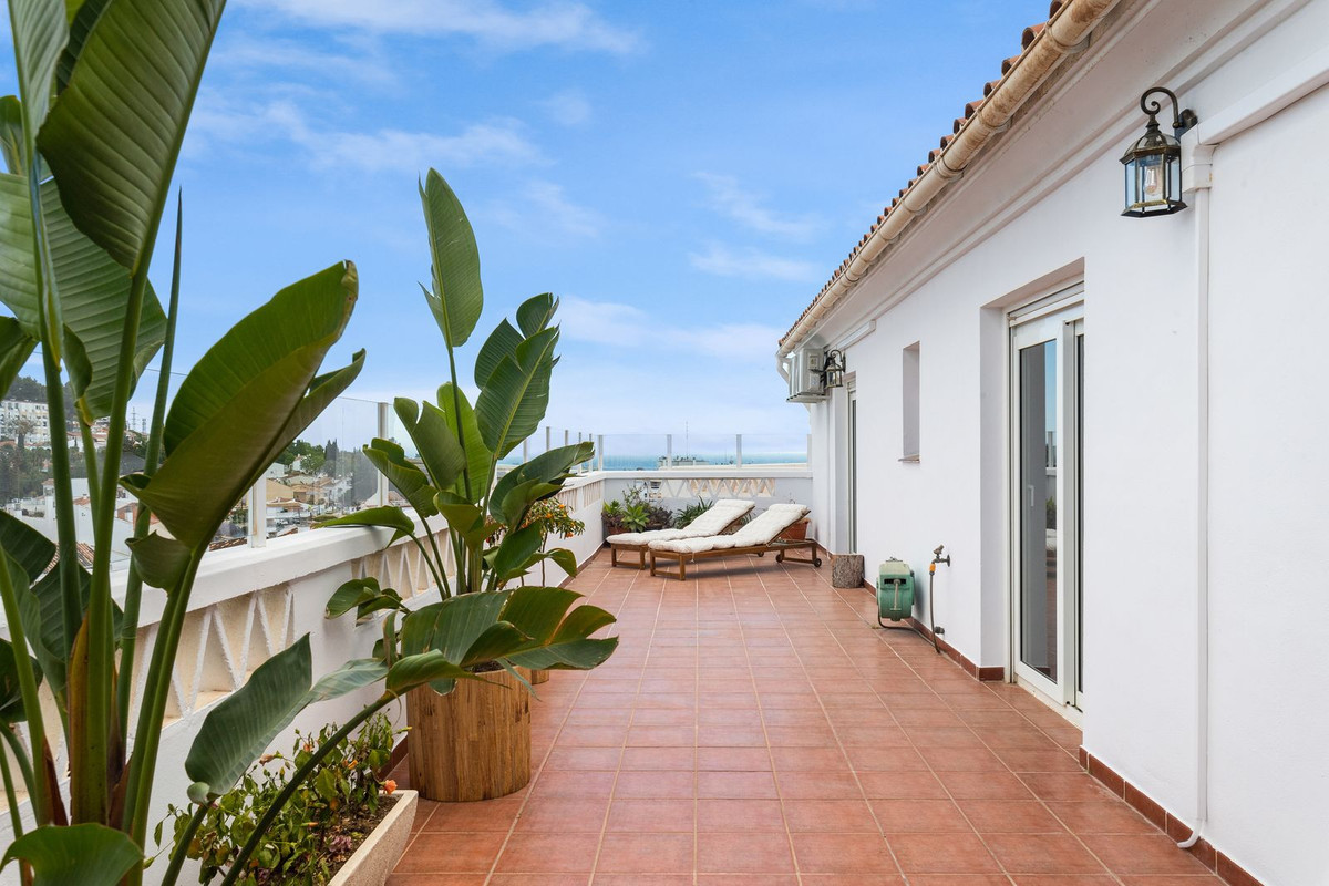 Rooftop terrace featuring two lounge chairs, potted plants, and a distant view of the sea.