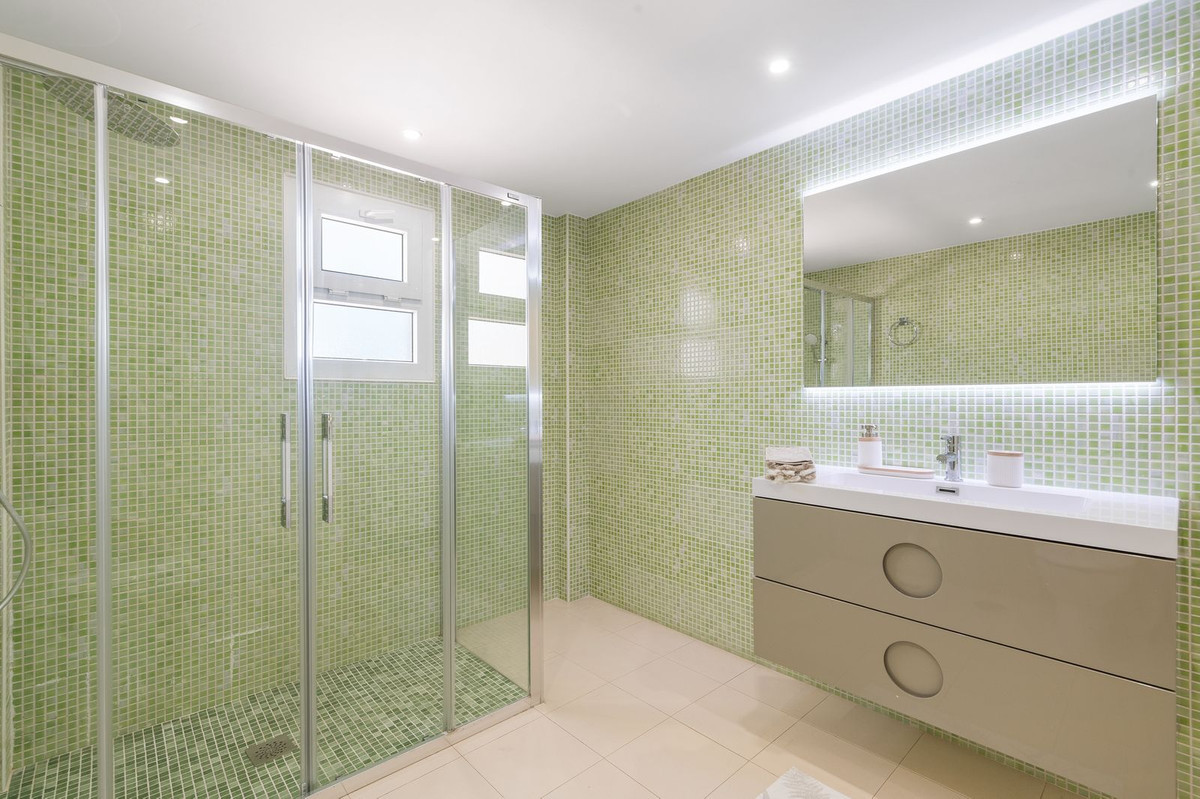 Bathroom with green mosaic tile walls, a glass shower enclosure, and a vanity with a lighted mirror.