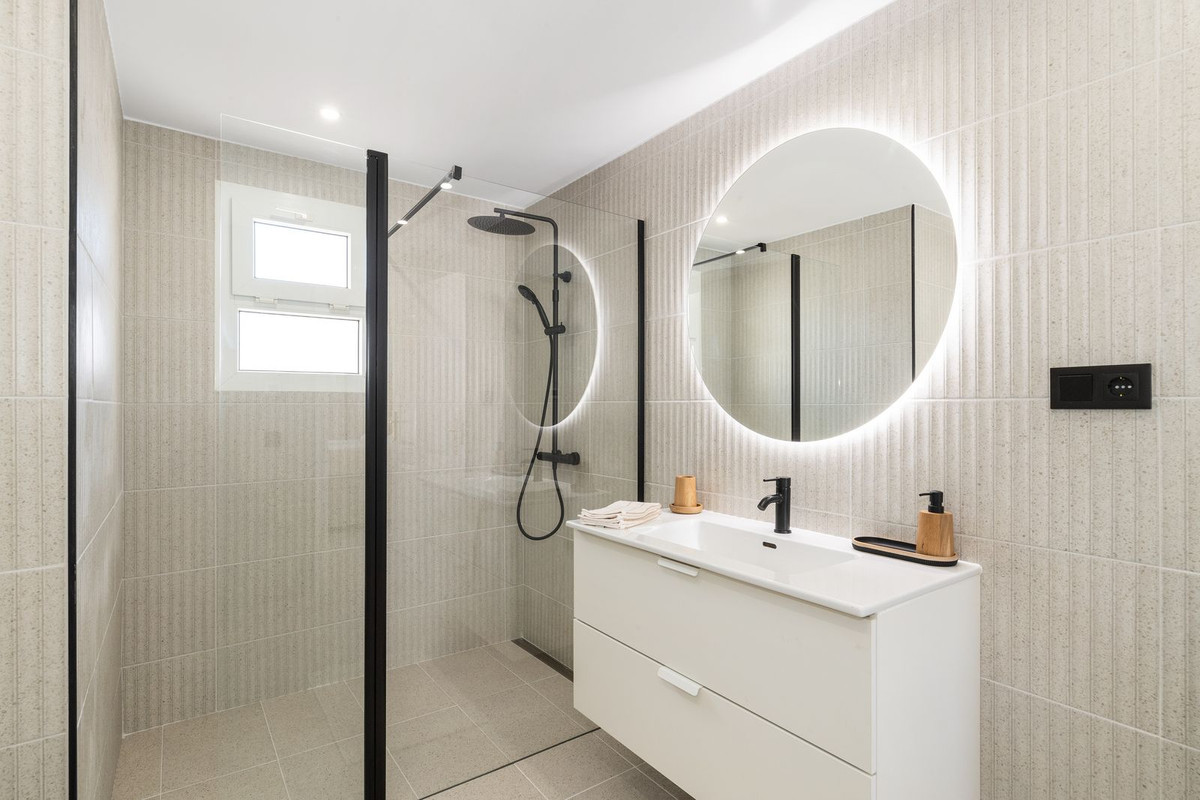 Bathroom with a walk-in shower, floating vanity, backlit round mirror, and tiled walls.