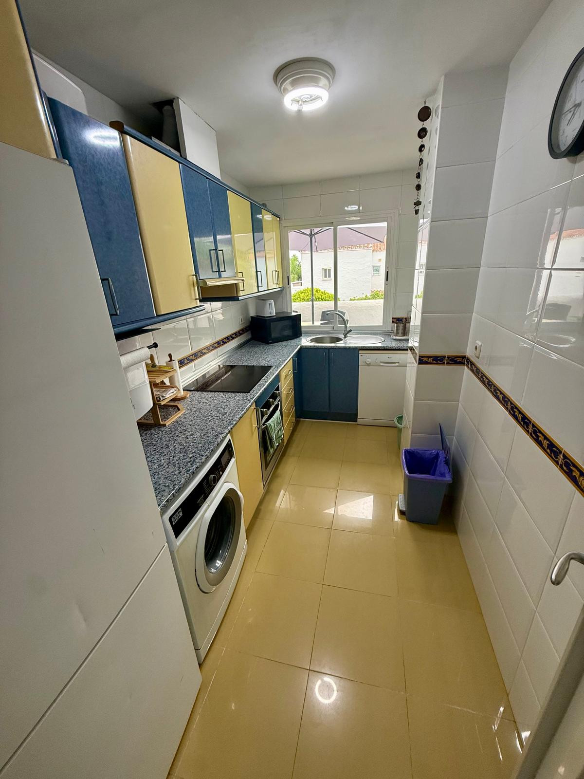 Narrow kitchen with yellow floor tiles, blue and yellow cabinets, and a white washing machine.