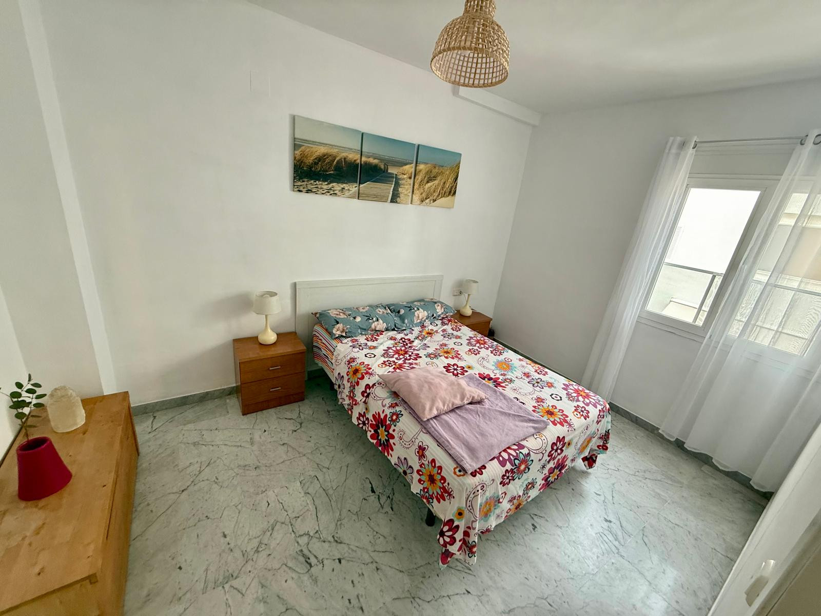 Bedroom with a queen-sized bed, white walls, and a three-panel artwork above the headboard.