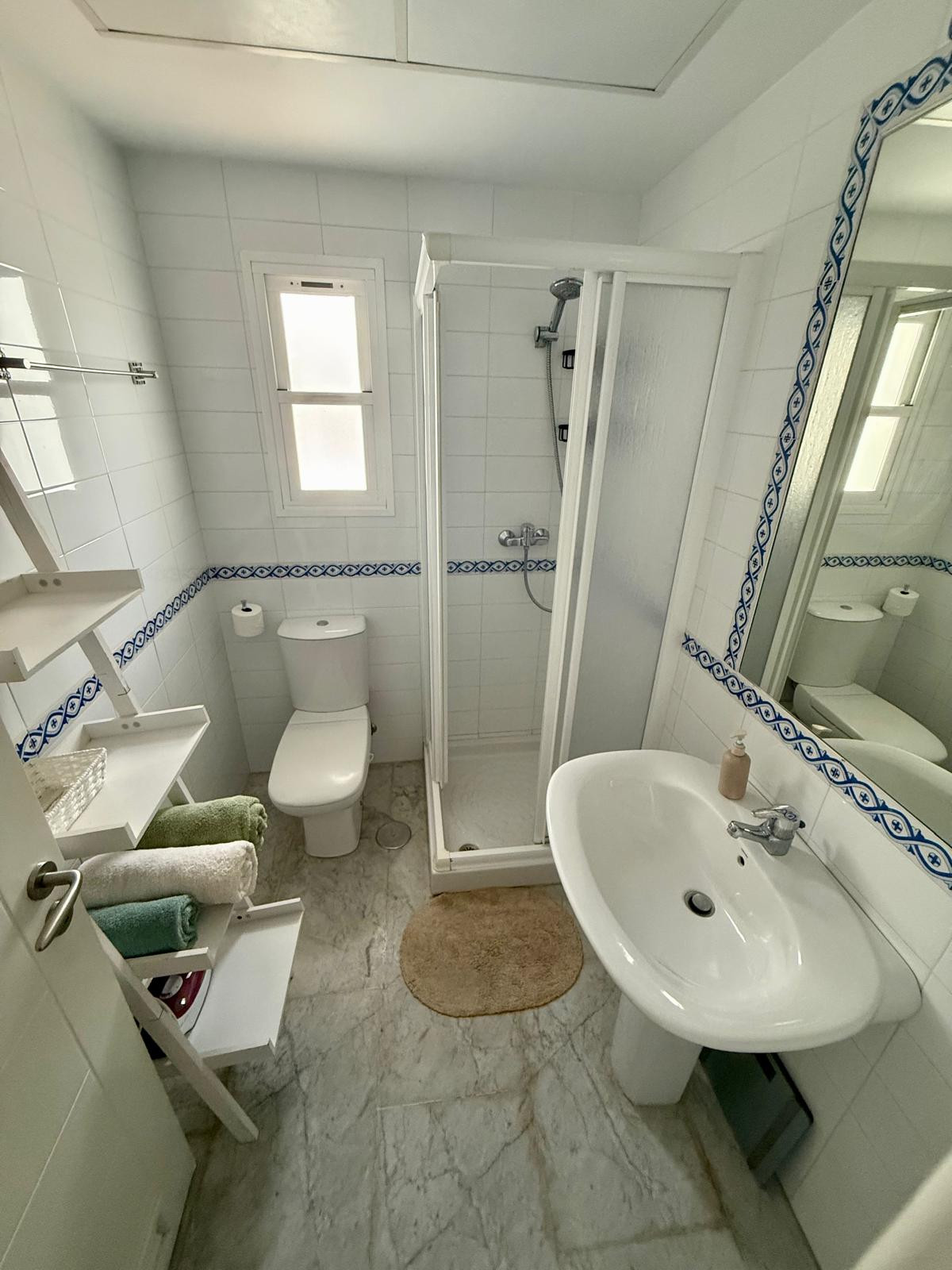 Bathroom with a pedestal sink, toilet, glass shower, and small frosted window. White tile walls.
