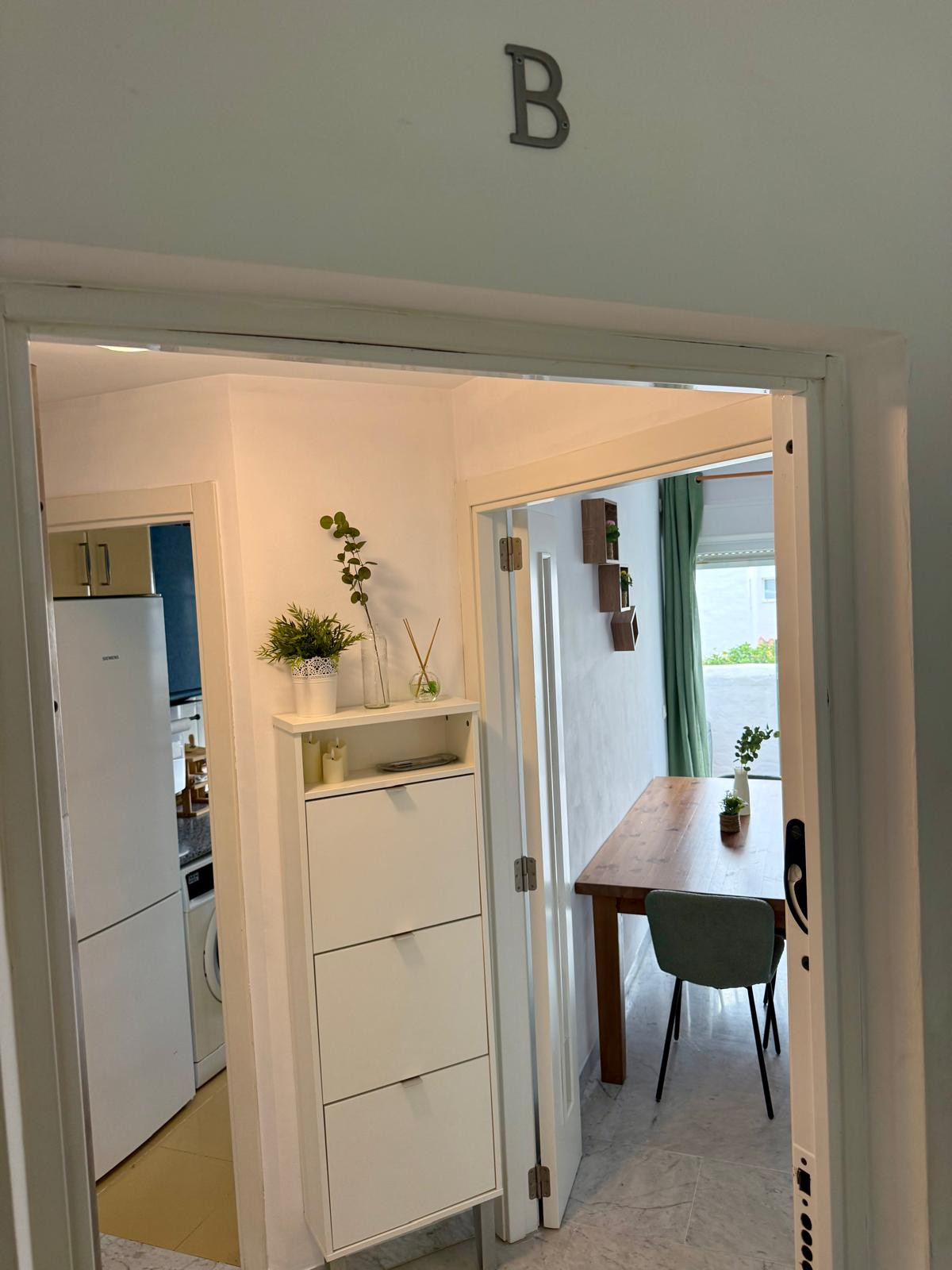 Hallway showing a shoe cabinet, a white refrigerator, and a glimpse into the living and dining areas.