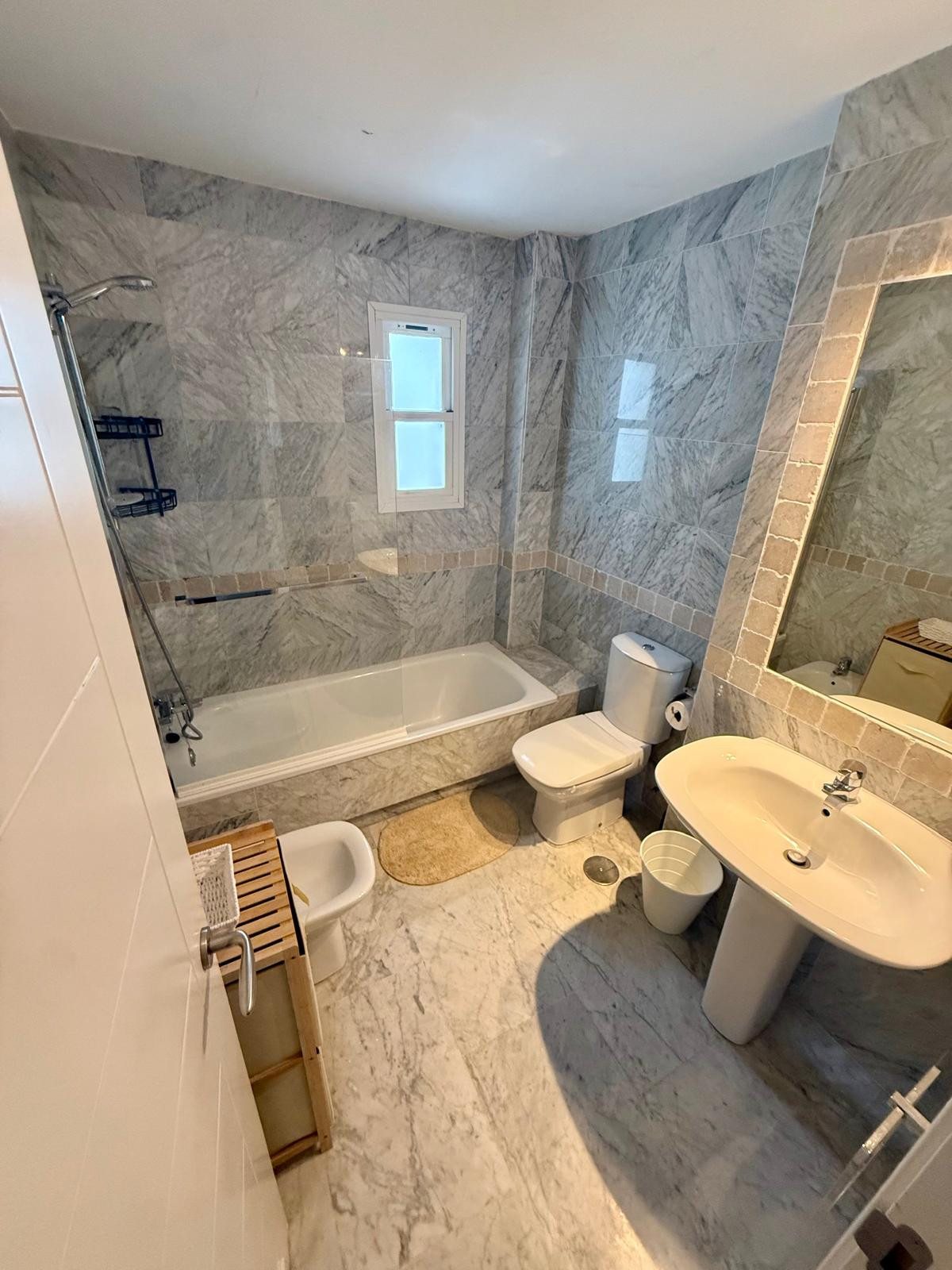 Bathroom with gray marble walls, a bathtub with shower, toilet, bidet, and pedestal sink.