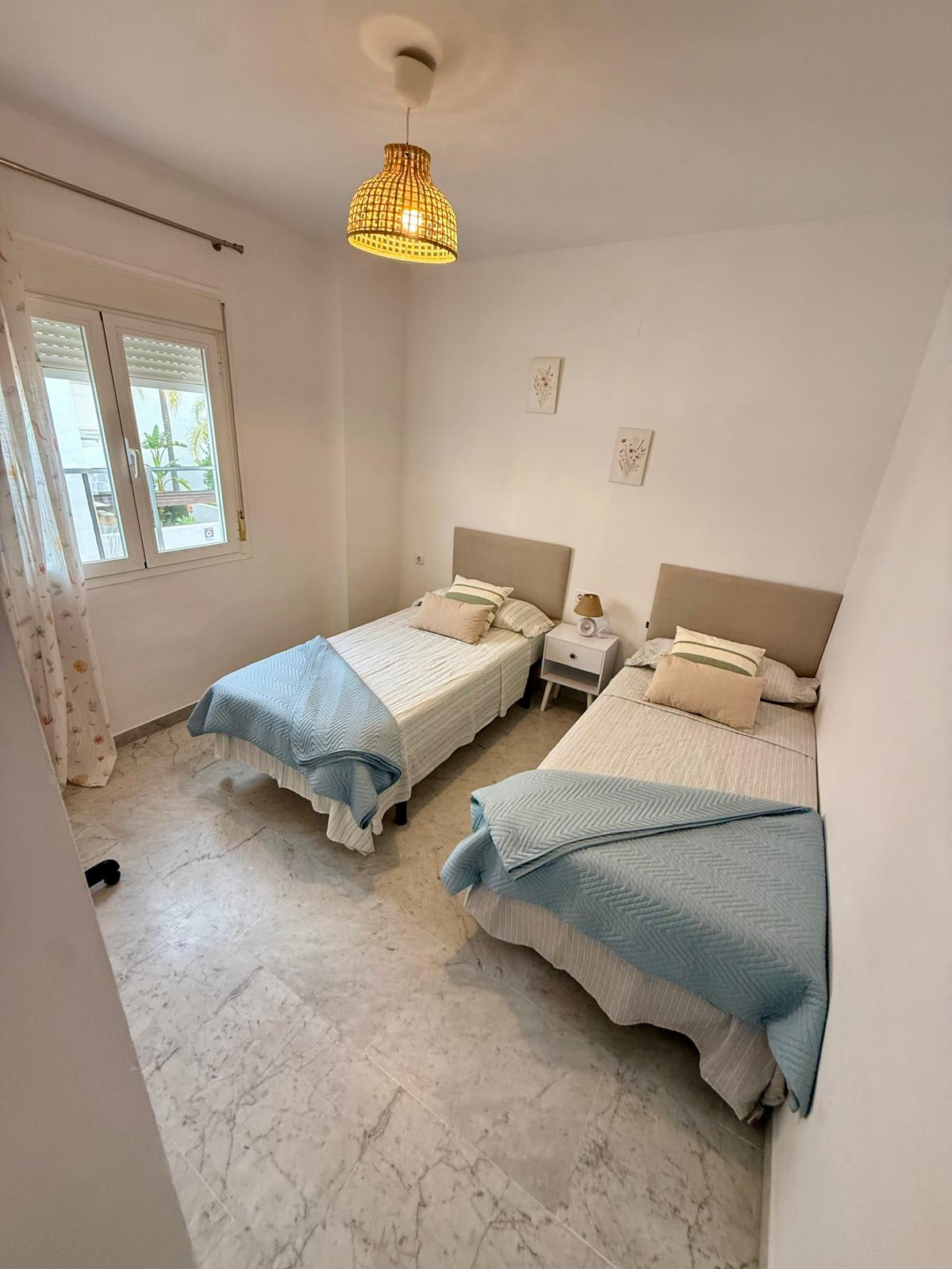 Bedroom with two single beds, a shared nightstand, and a rattan pendant light fixture.