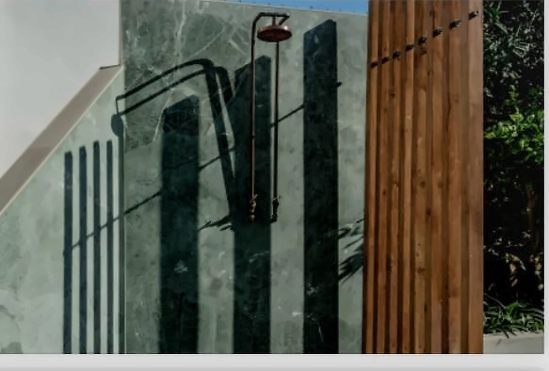 Outdoor shower with a dark marble panel, copper showerhead, and vertical wooden slatted screen.