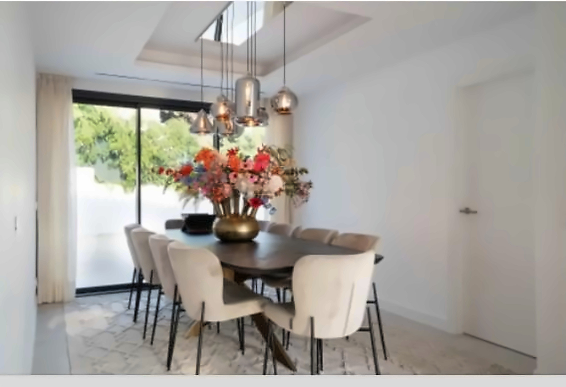 Dining room with large table, ten chairs, hanging light fixtures, and glass doors to garden.