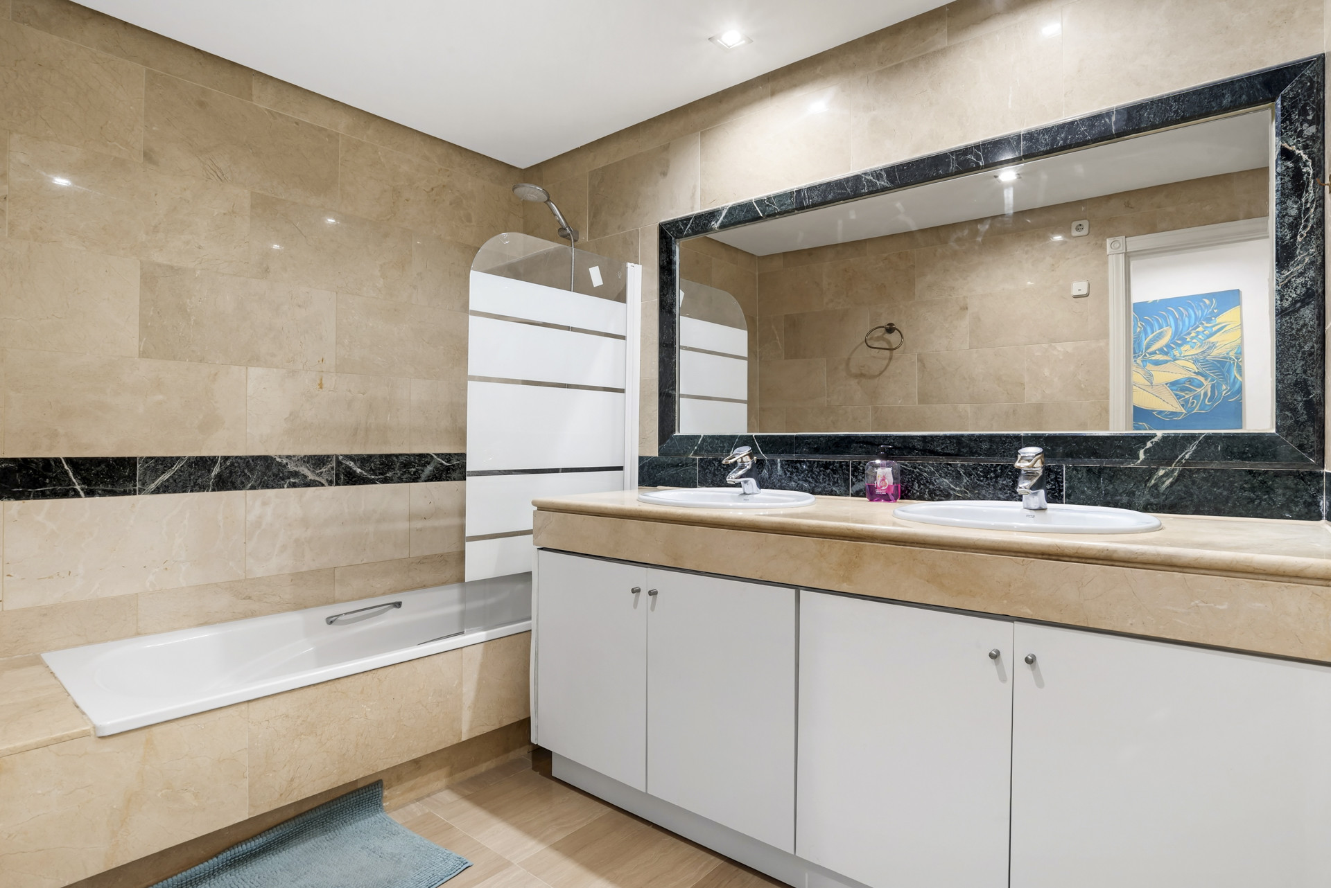 Bathroom with a double vanity, a large mirror, and a bathtub with an overhead shower.