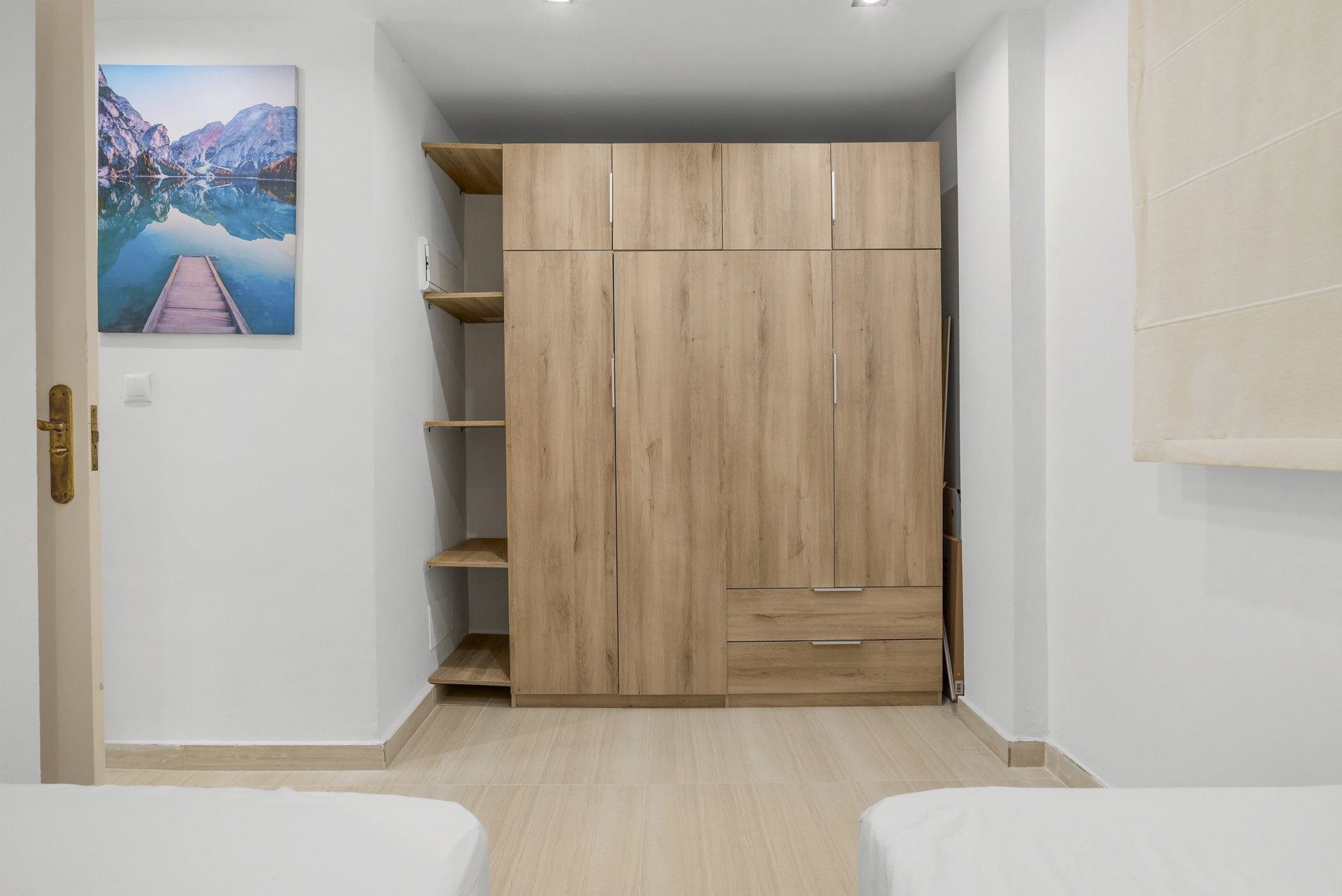 Bedroom wall with a large wooden built-in wardrobe, open shelves, and a scenic framed artwork.