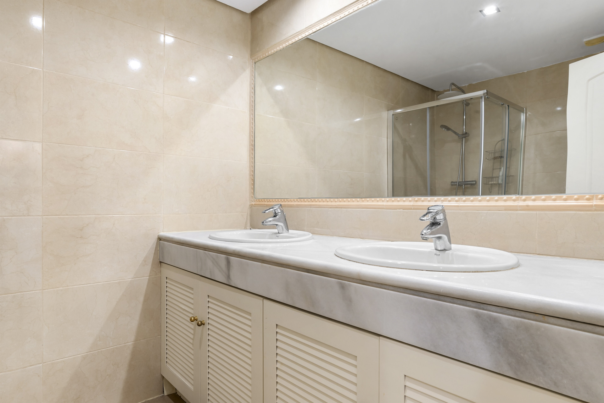 Bathroom with a double vanity featuring a white marble countertop, twin sinks, and a large mirror.