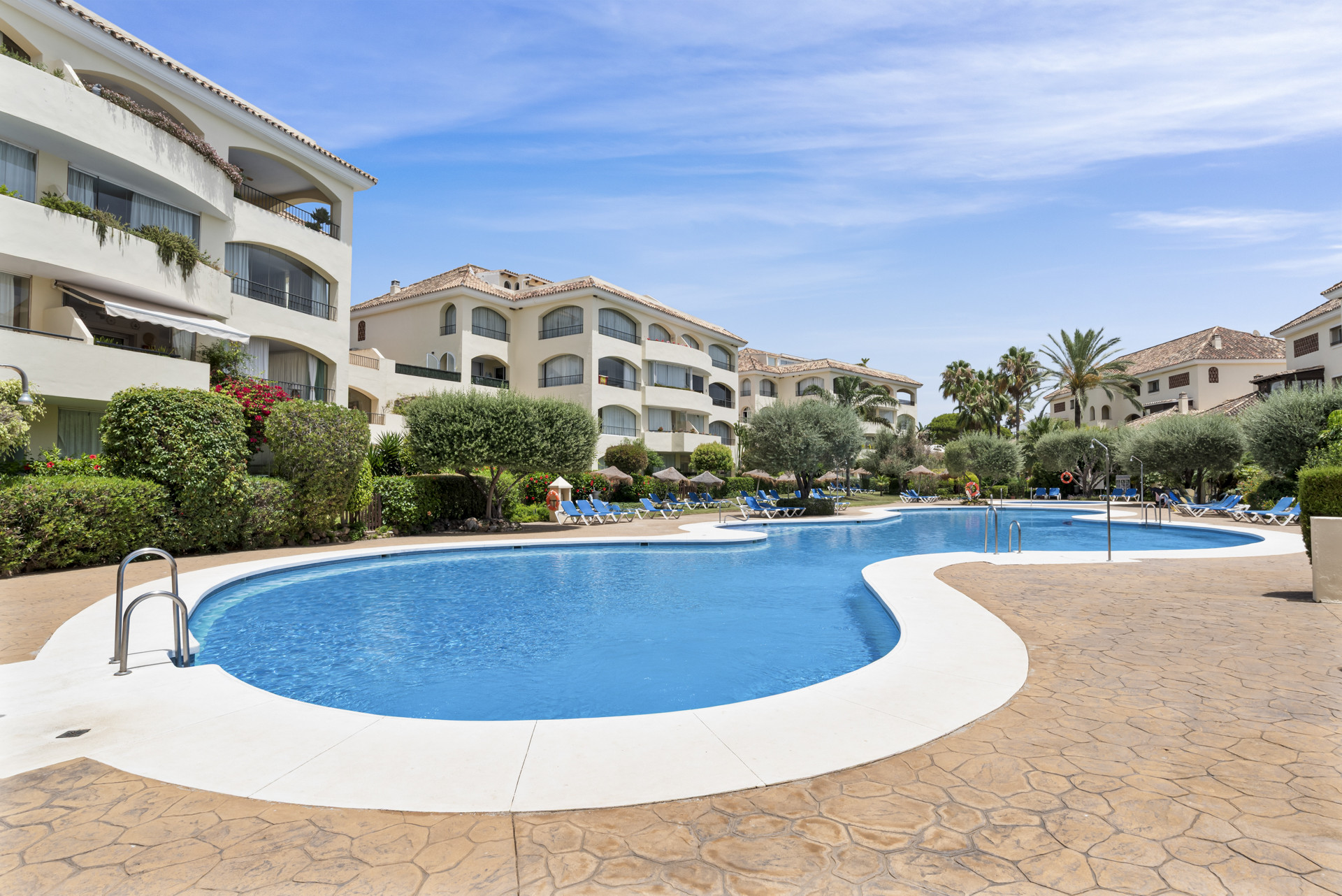 Angled shot of a resort-style swimming pool with white coping, surrounded by stone paving and apartment buildings.