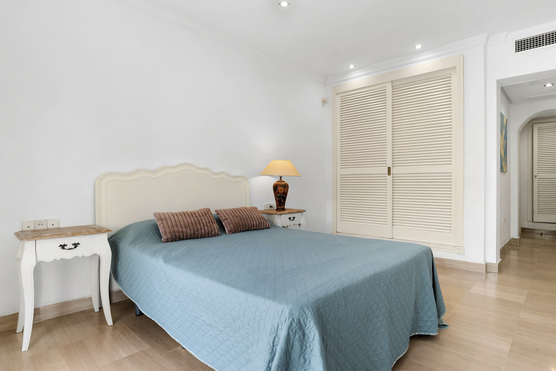 Bedroom with a queen-sized bed, white furniture, and a built-in louvered wardrobe on the right.