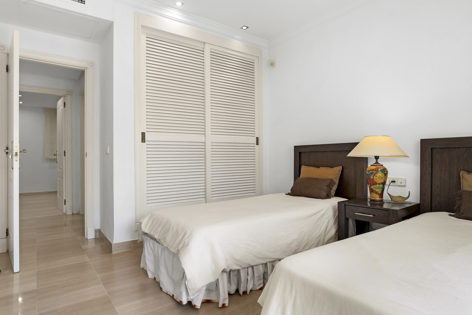 Bedroom with two single beds, dark wood headboards, a bedside table, and louvered closet doors.