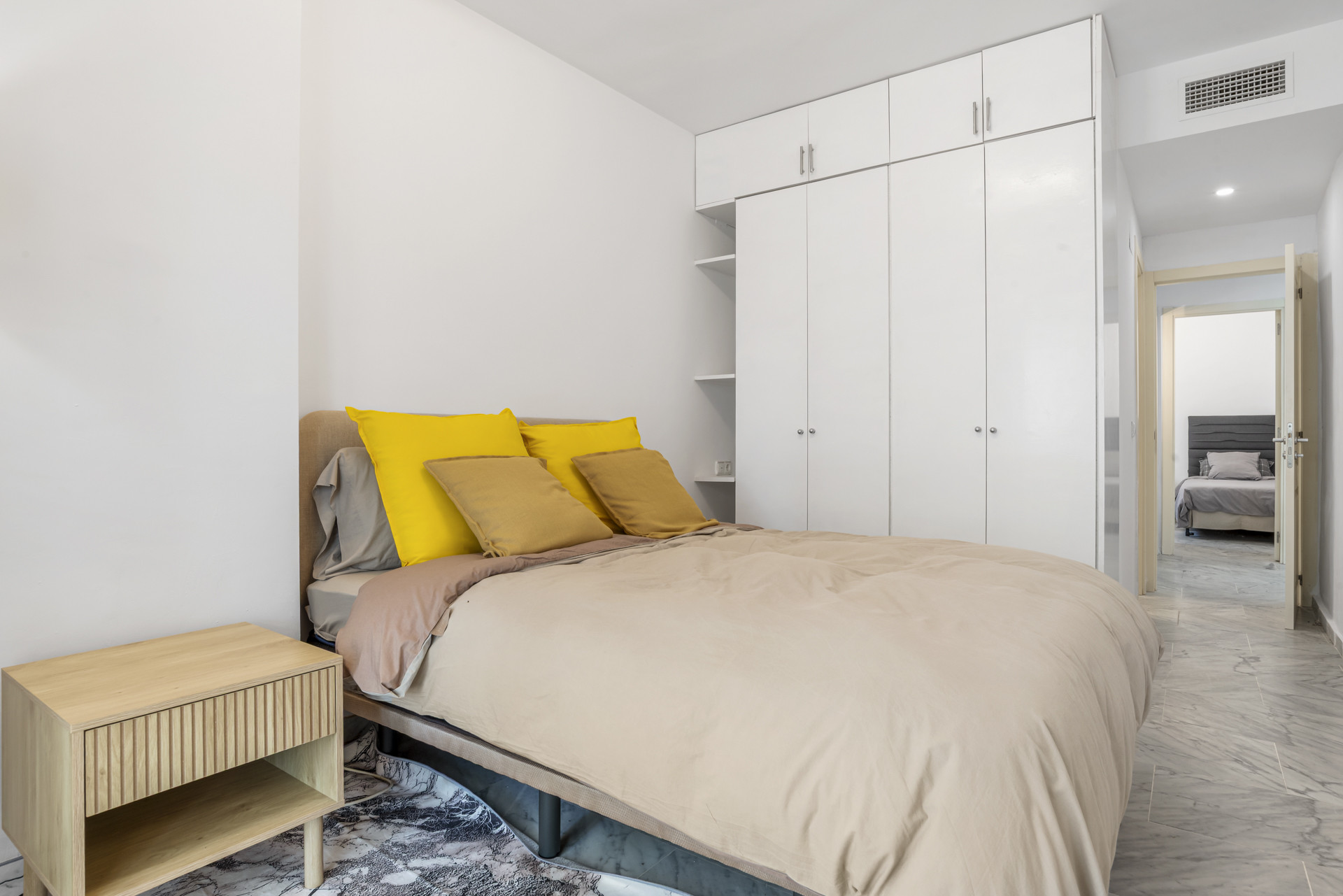 Bedroom with double bed, yellow and gold pillows, light wood nightstand, and white built-in wardrobe.