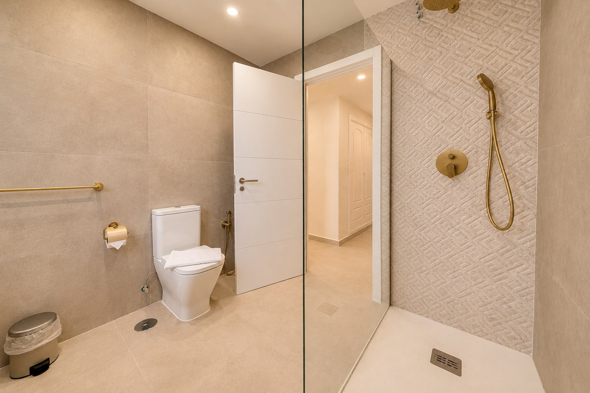Bathroom with a white toilet, gold shower fixtures, and an open doorway leading to a hallway.