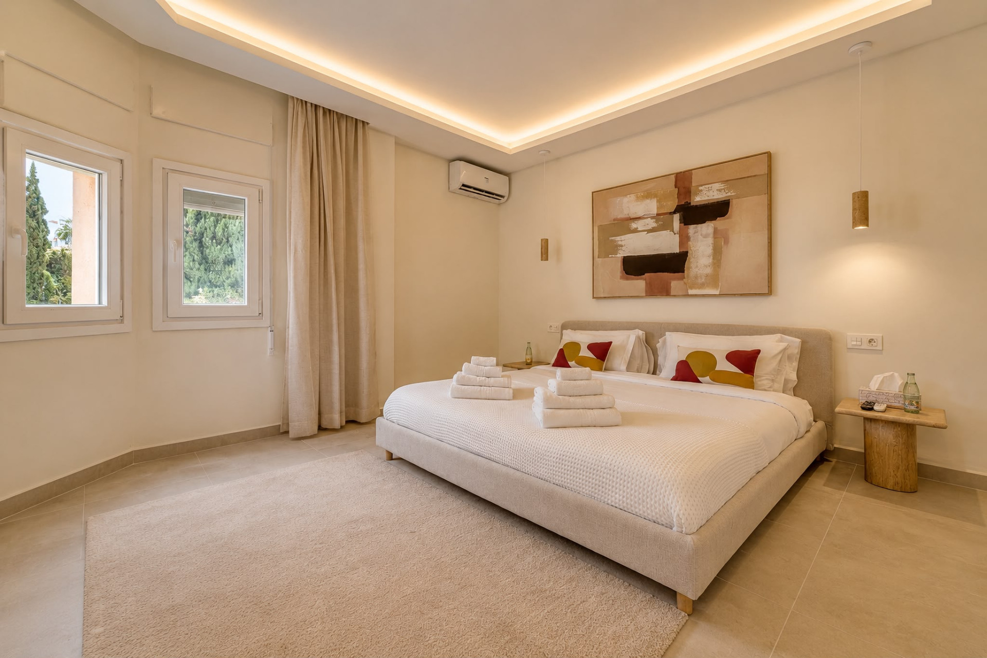 Bedroom with a large bed, abstract art, two windows with drapes, and recessed lighting in the ceiling.