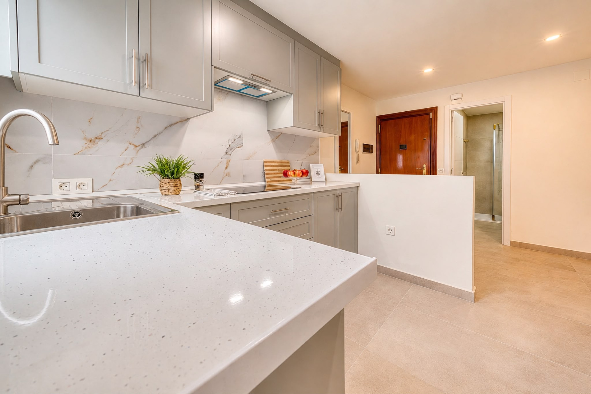 Kitchen counter with sink and stovetop, facing a partial wall, with a hallway and doorway visible beyond.