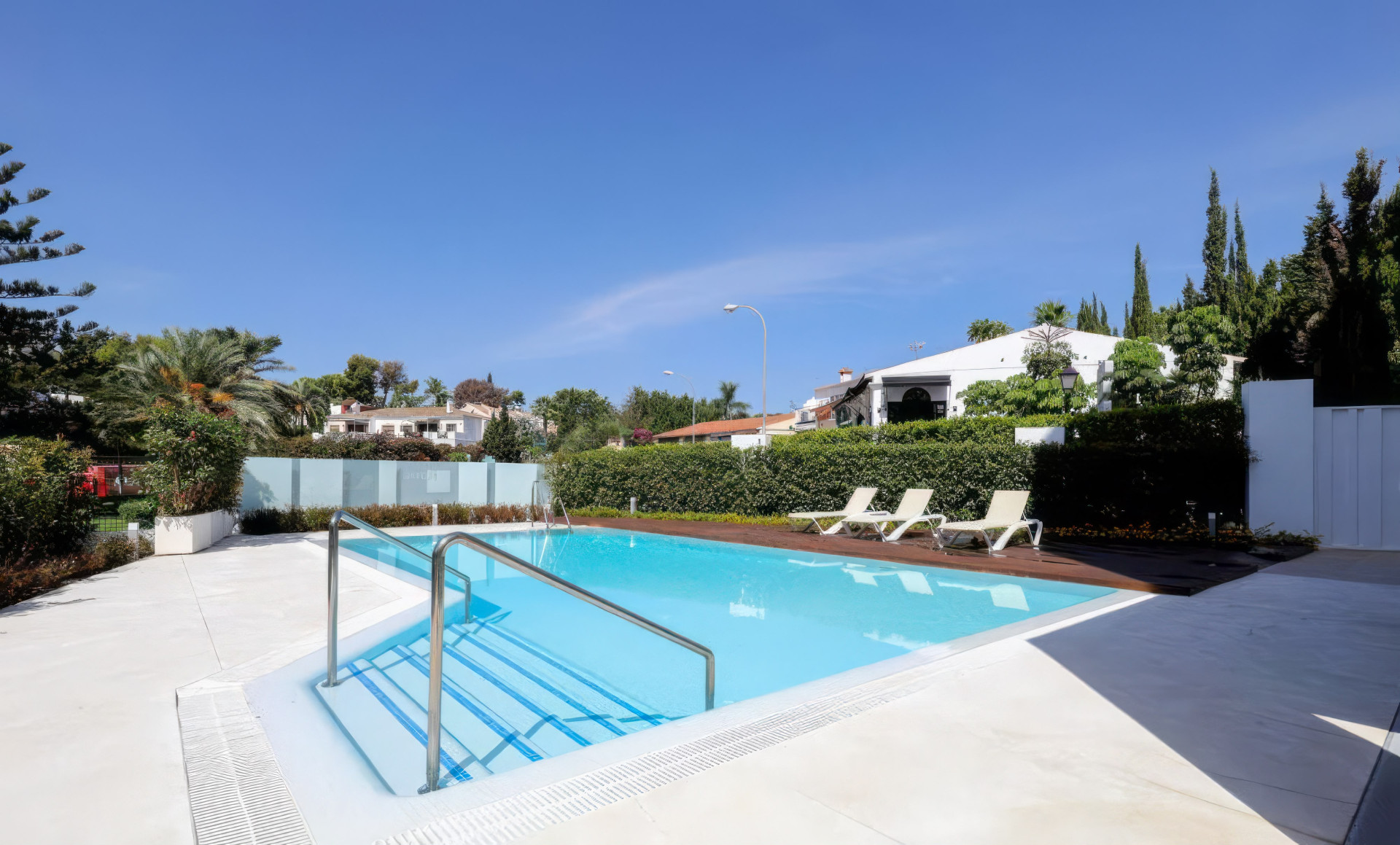 Wide view of an outdoor swimming pool with integrated steps and several lounge chairs.