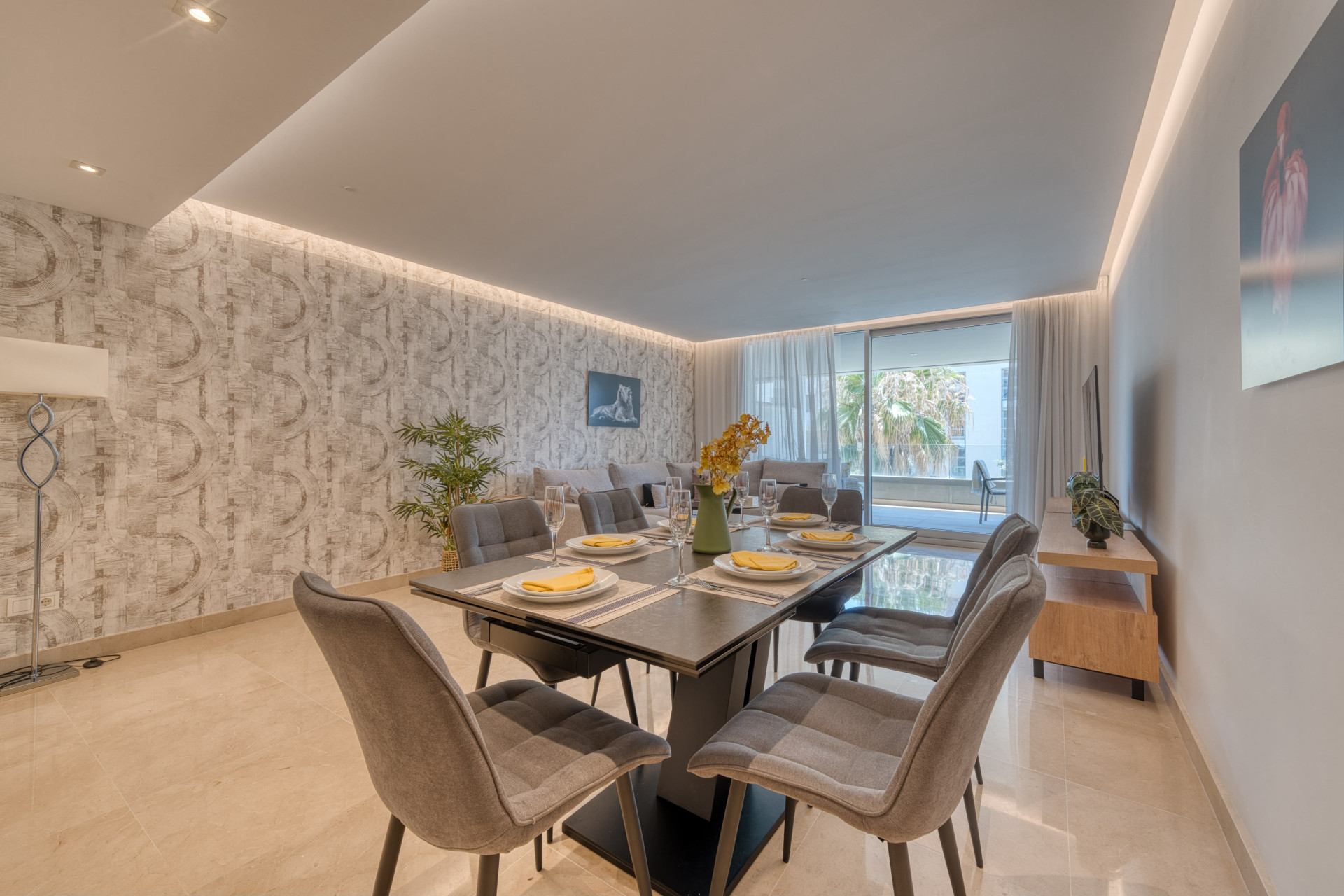 Dining area with a set table for six, viewed towards the living room and balcony access.