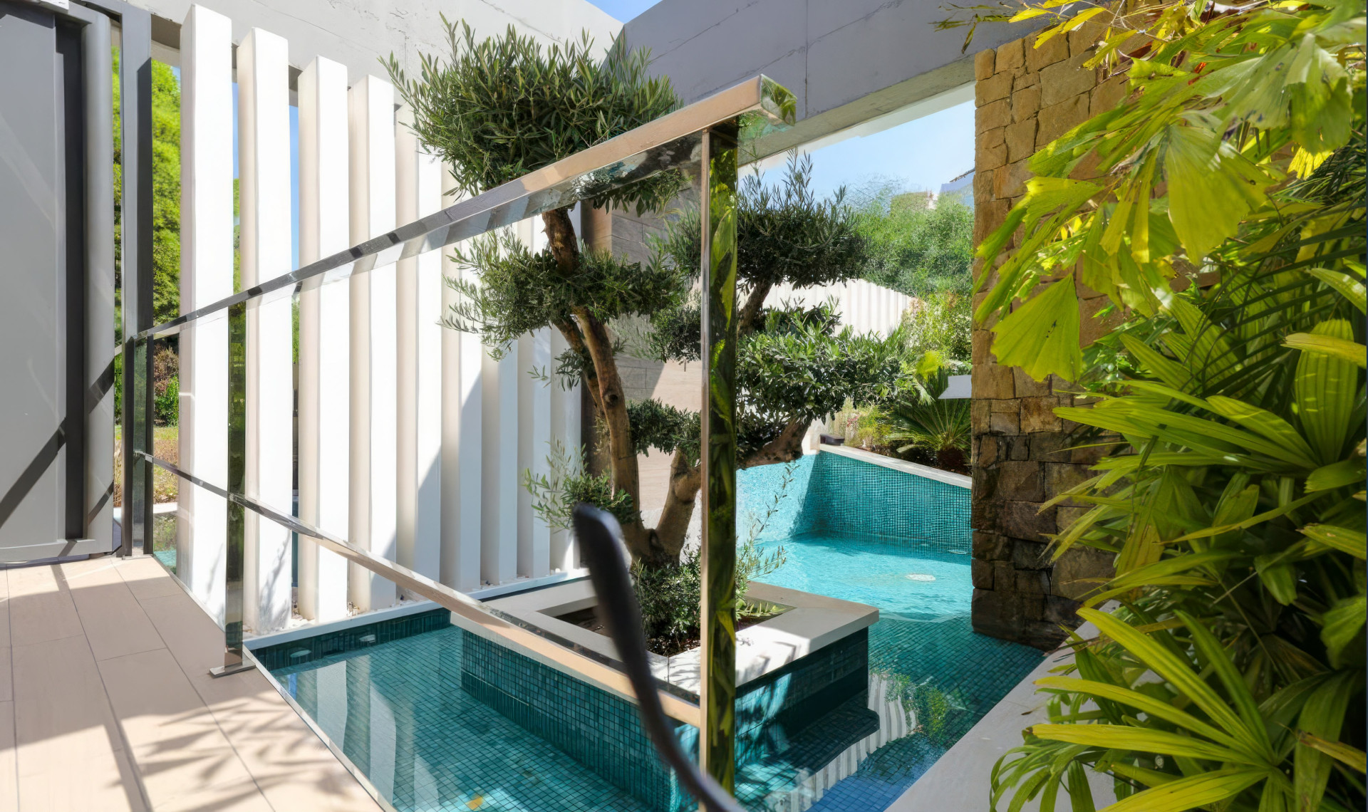 Outdoor water feature with a small tree, tiled pool, and vertical white slat wall.