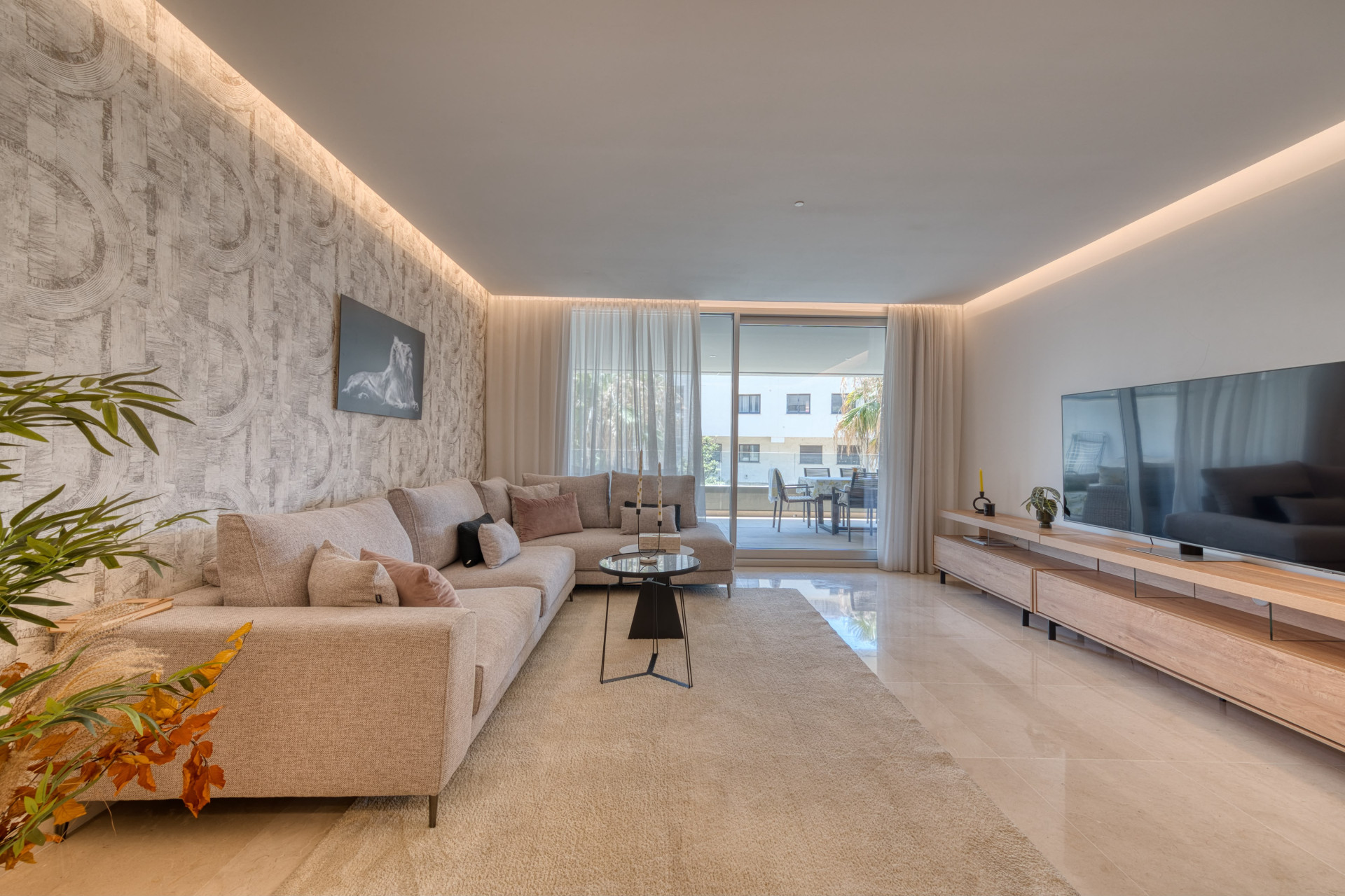 Living room featuring a textured accent wall, large sectional sofa, television, and outdoor patio beyond.