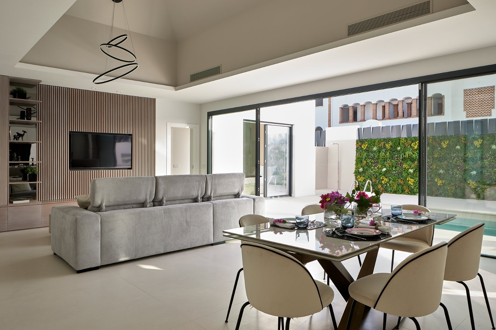 Spacious living room with gray sofa and dining table next to large sliding glass doors overlooking a pool.