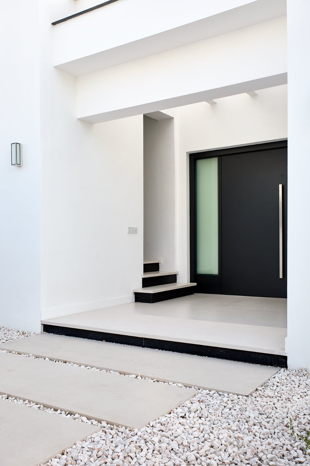 Contemporary villa entrance with a dark front door, stone steps, and a gravel and concrete pathway.