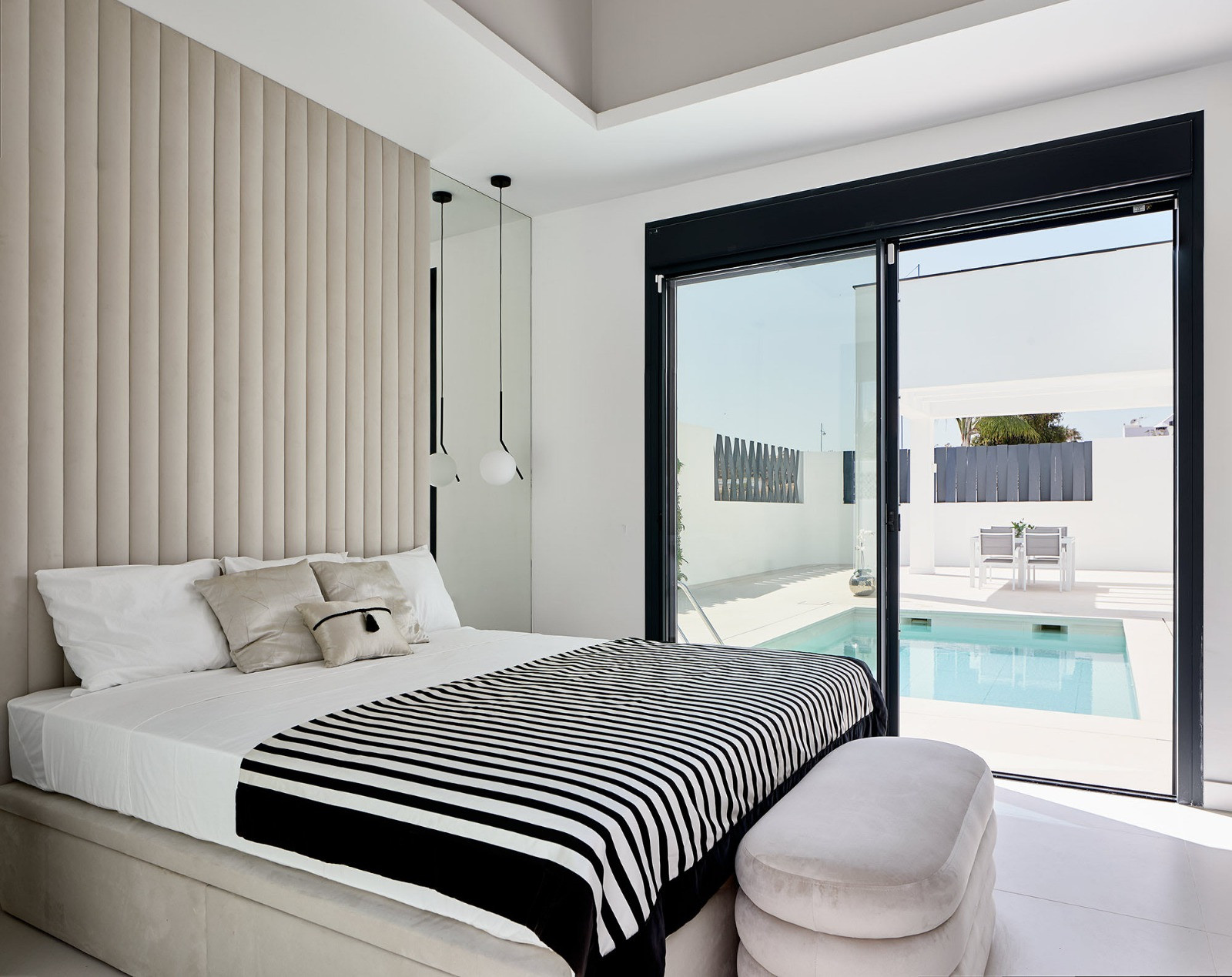 Bedroom with a large bed, striped throw, upholstered headboard, and sliding glass doors to a pool.