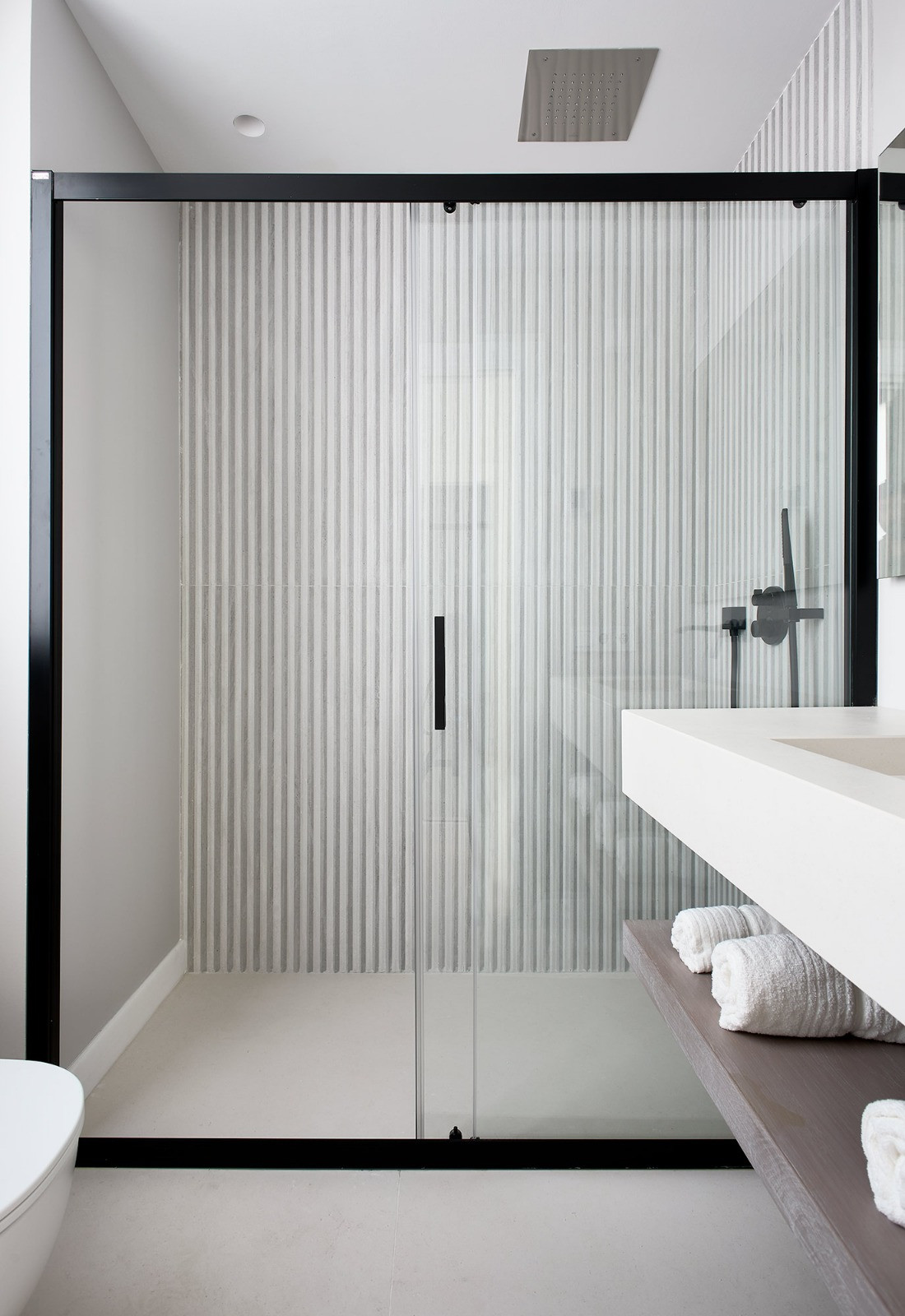 View of a walk-in shower with black frame, glass door, rain showerhead, and patterned wall tiles.