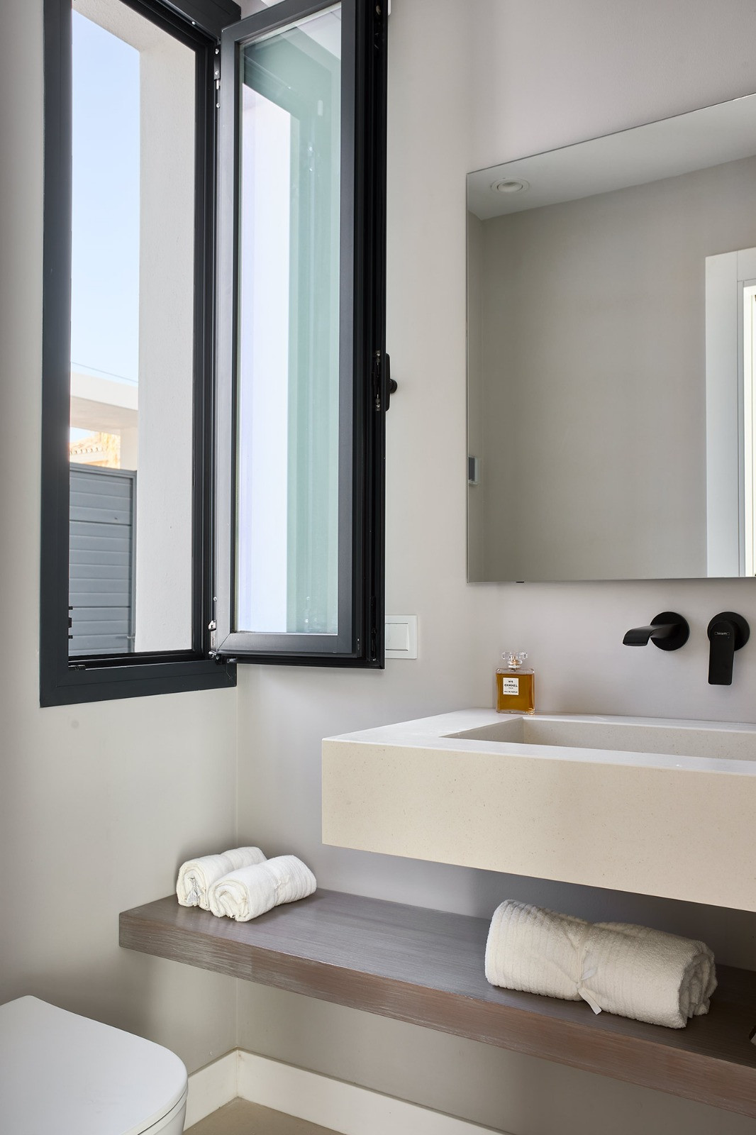 Bathroom with a rectangular mirror above a light vanity, a black faucet, and an open casement window.
