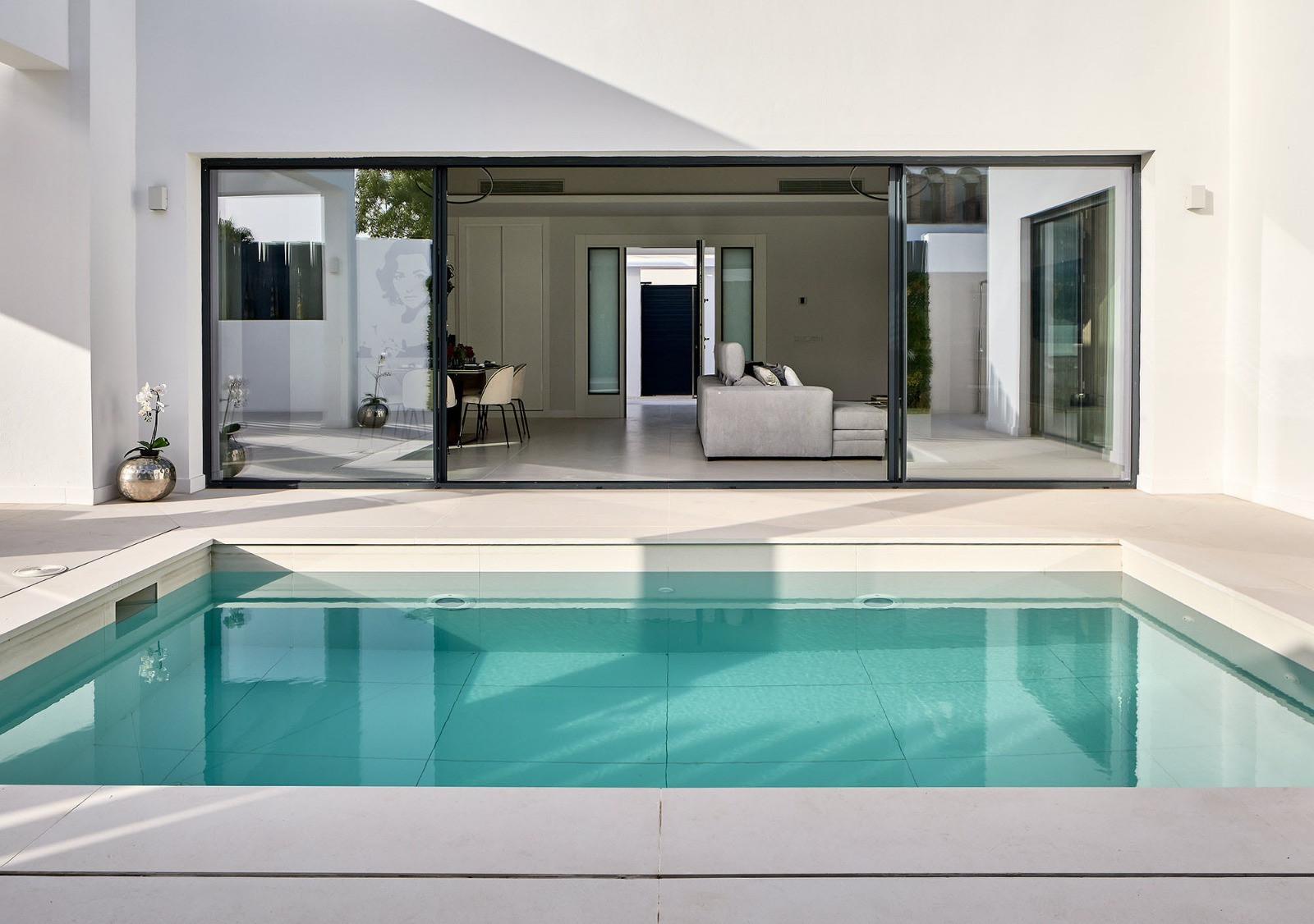 Outdoor pool area with a white tiled patio and large sliding glass doors opening to an indoor living space.