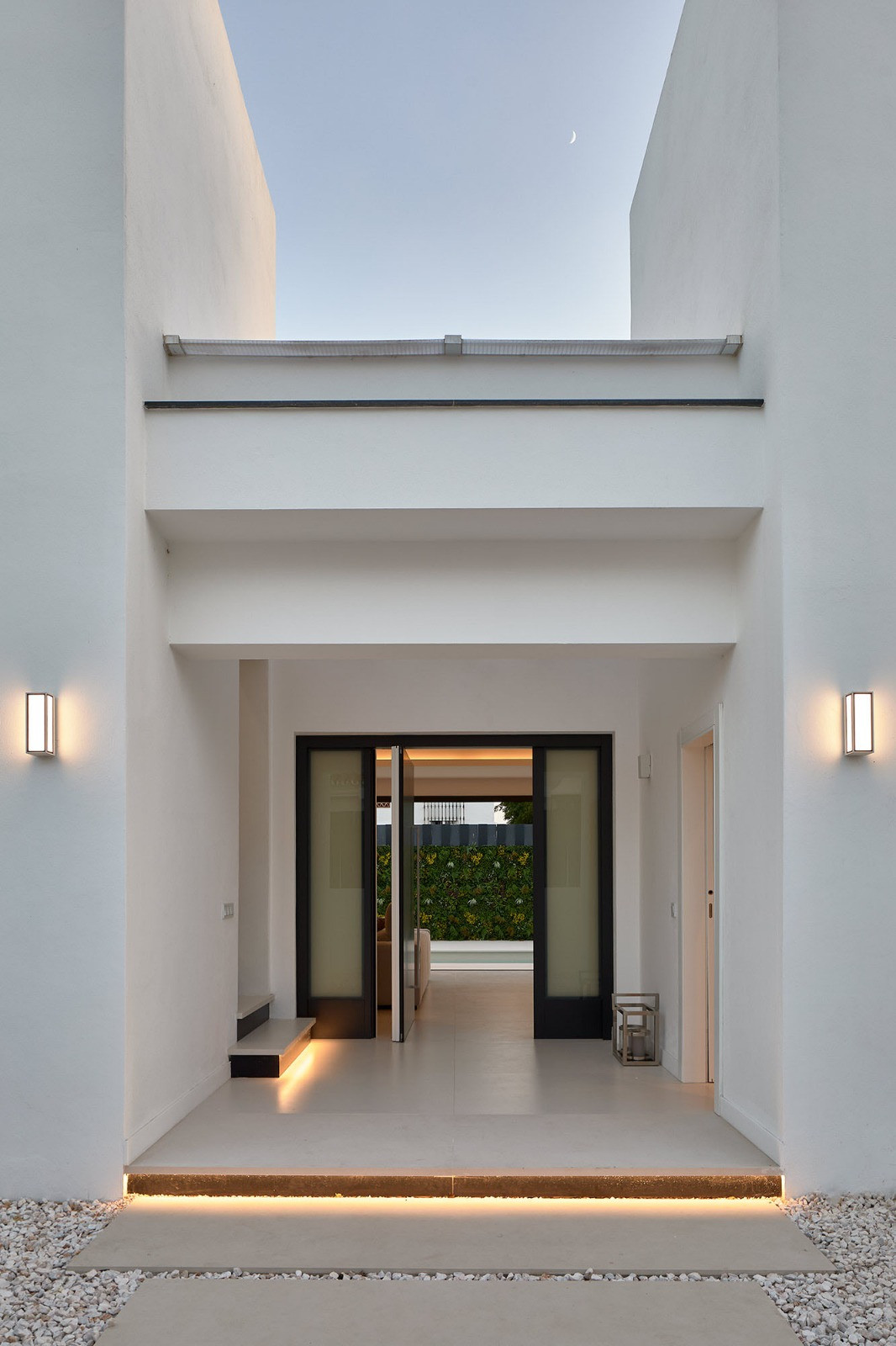 Night view of a modern villa entrance with illuminated steps, sconces, and glass doors to an interior space.