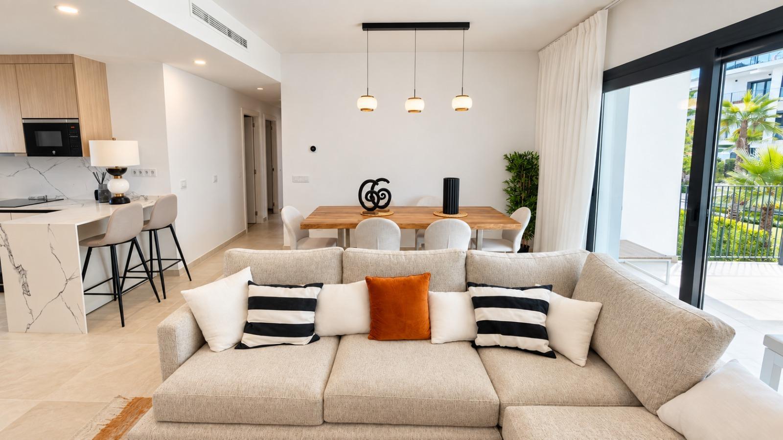 Open plan living area showing a beige sofa, dining table, and a kitchen island with bar stools.