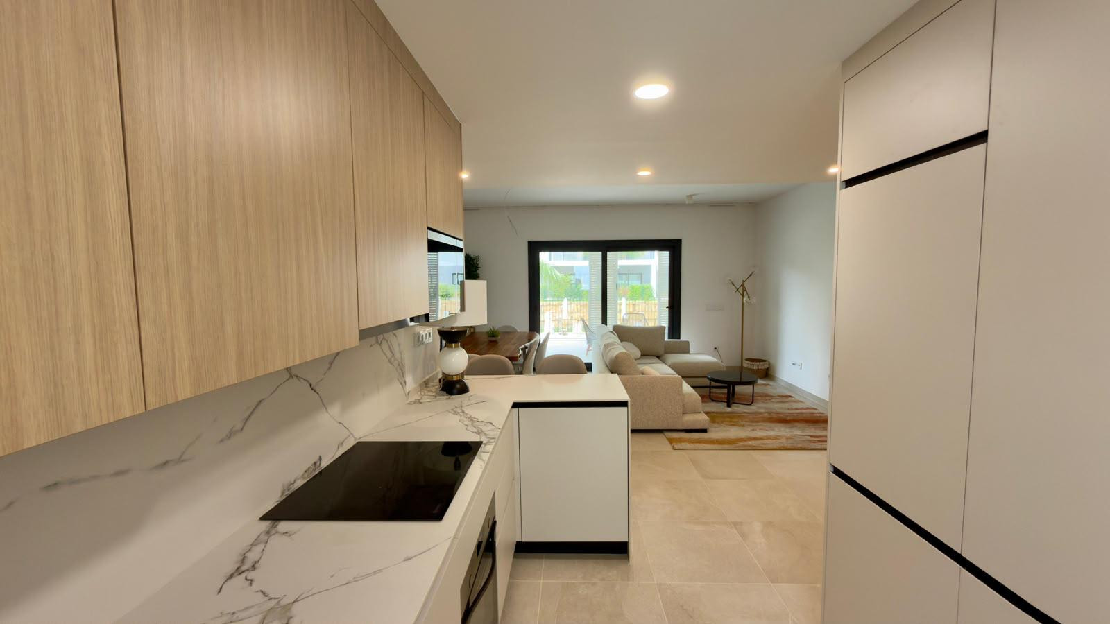Kitchen with marble countertops, wooden cabinets, and a view into the living room with a sofa and dining table.