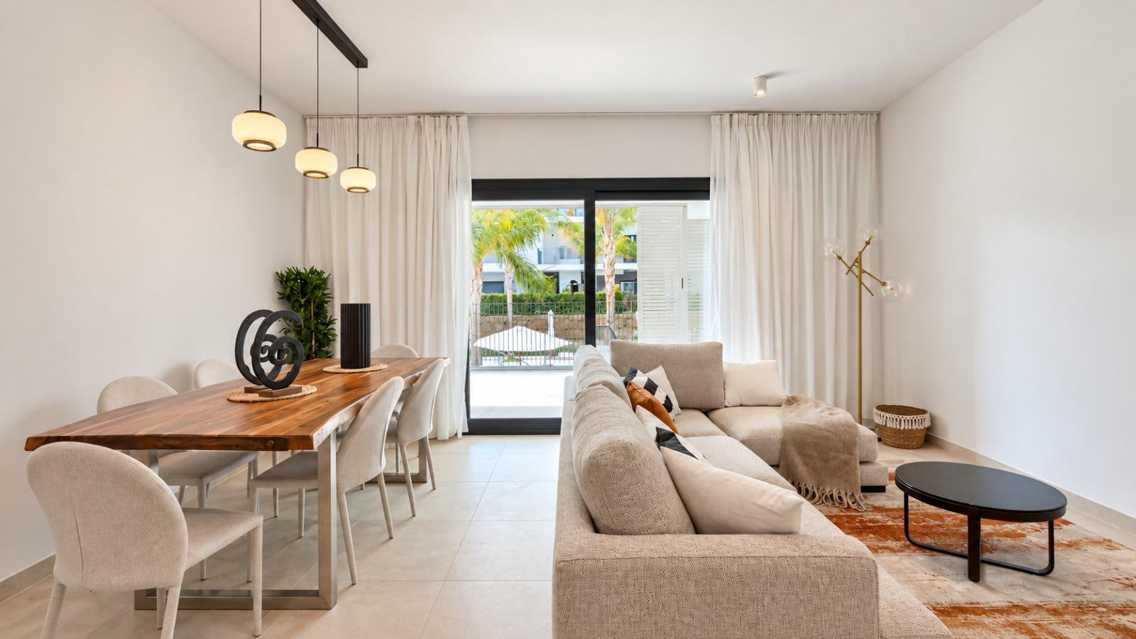 Living and dining room with a large sofa, wooden dining table, and glass sliding doors to an outdoor area.