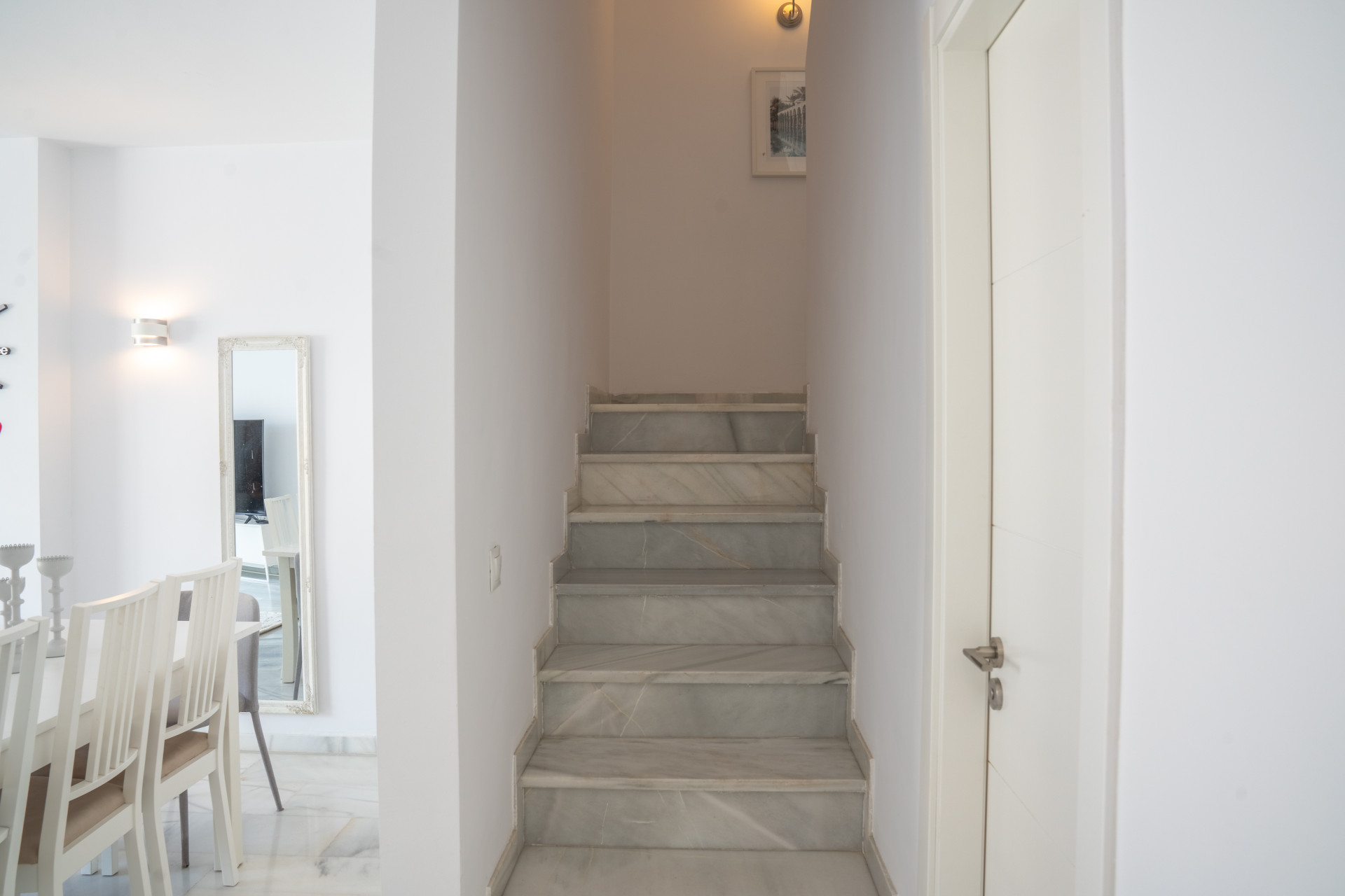 View of a marble staircase and a white door, with a dining area partially visible on the left.