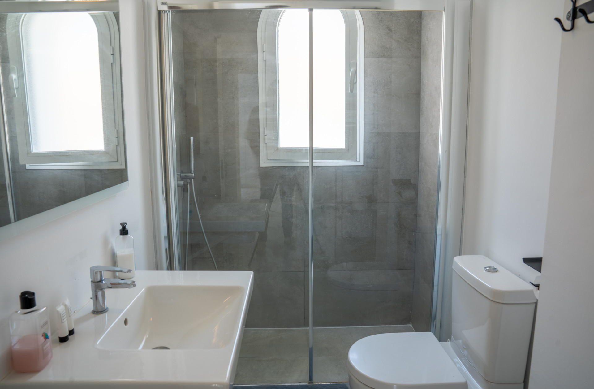 Modern bathroom with a glass shower stall, white sink with faucet, toilet, and an arched window.