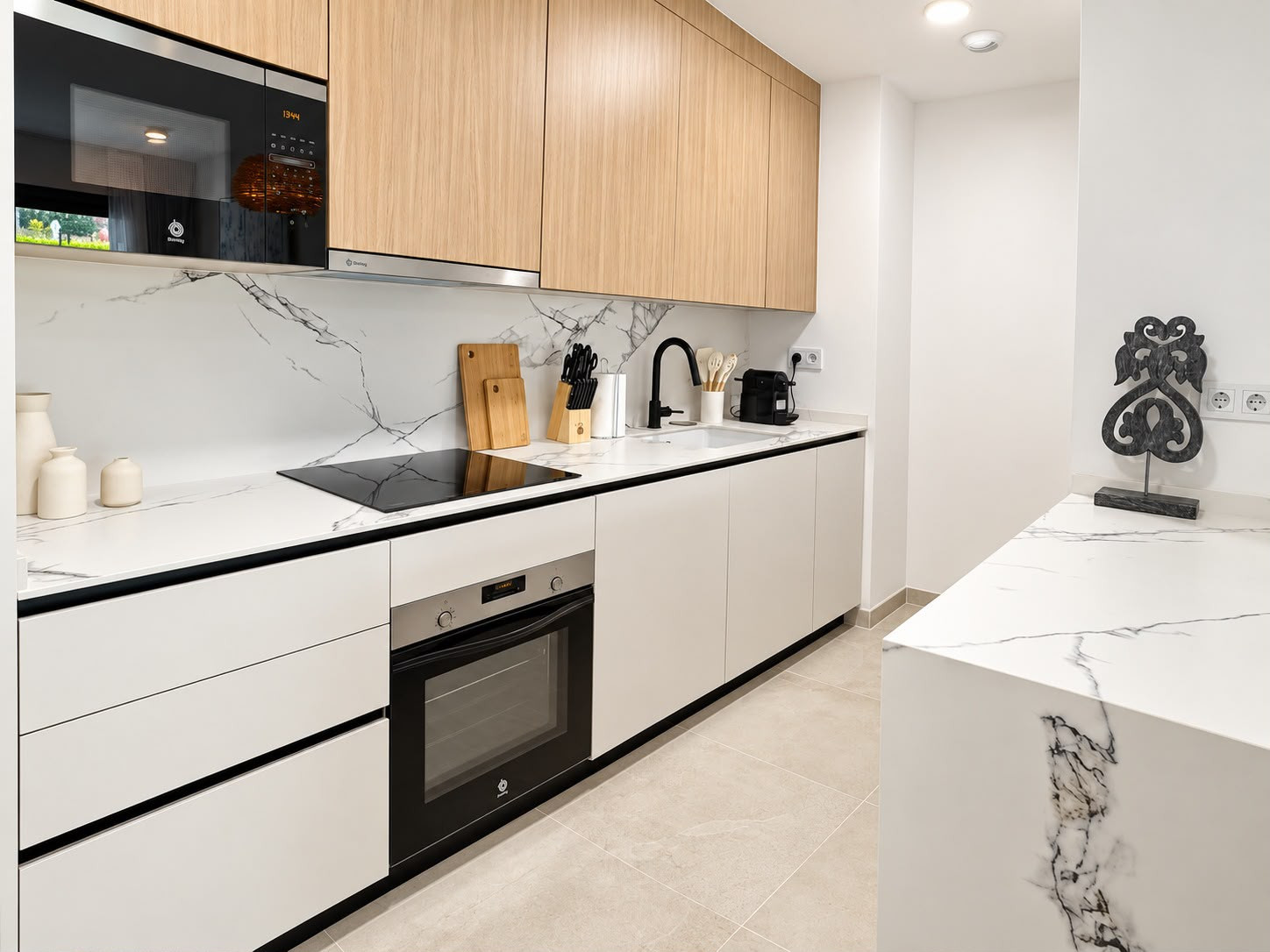 Kitchen with black cooktop and oven, marble backsplash, and white cabinets with wood uppers.