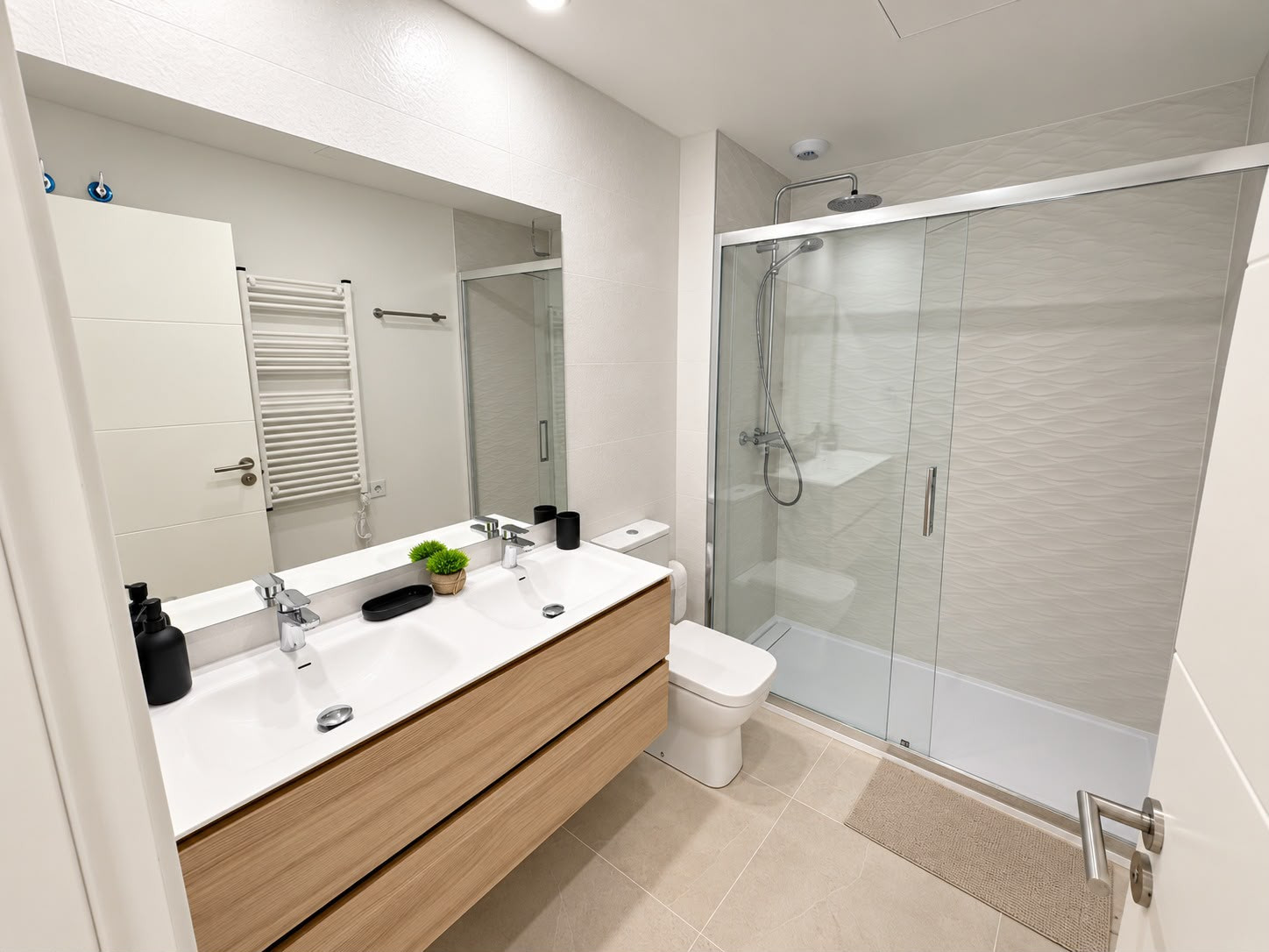 Bathroom with a double vanity, large mirror, and glass-enclosed shower on the right.