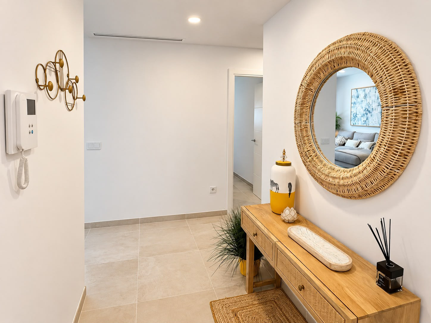 Entryway with a wooden console table, round rattan mirror, coat rack, and intercom system.