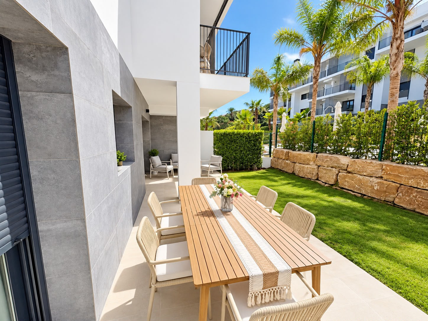 View of the outdoor patio with a large wooden dining table and chairs, facing a lush garden.