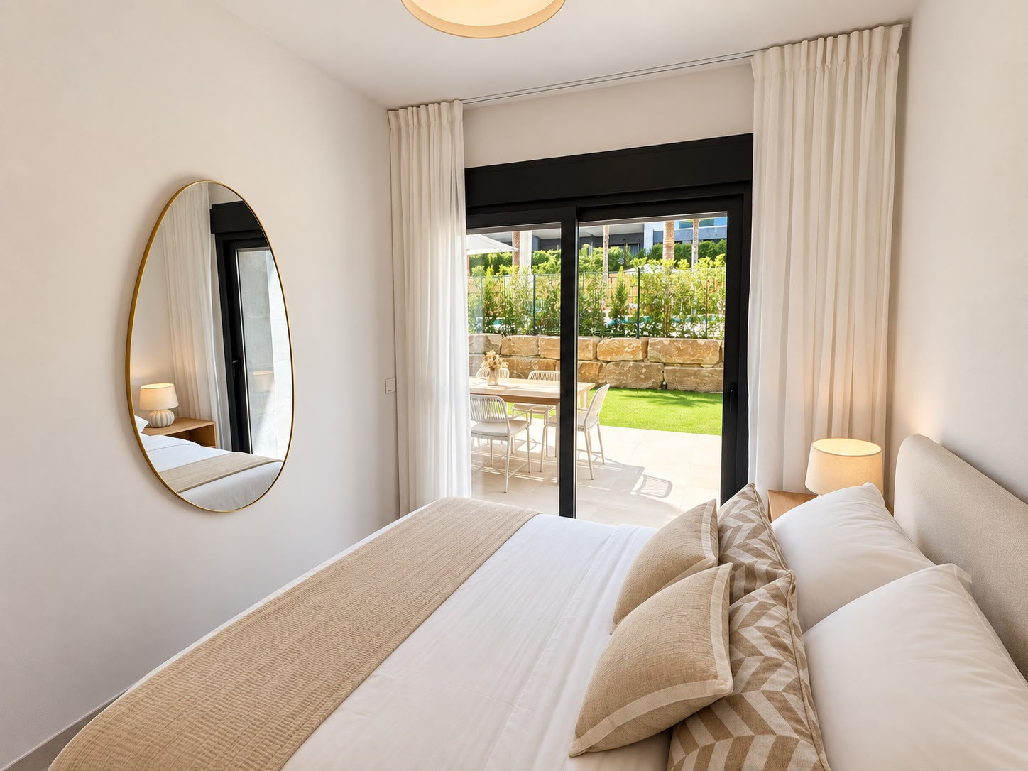 Bedroom with a queen-sized bed, gold framed mirror, and sliding glass doors opening to a covered outdoor patio.
