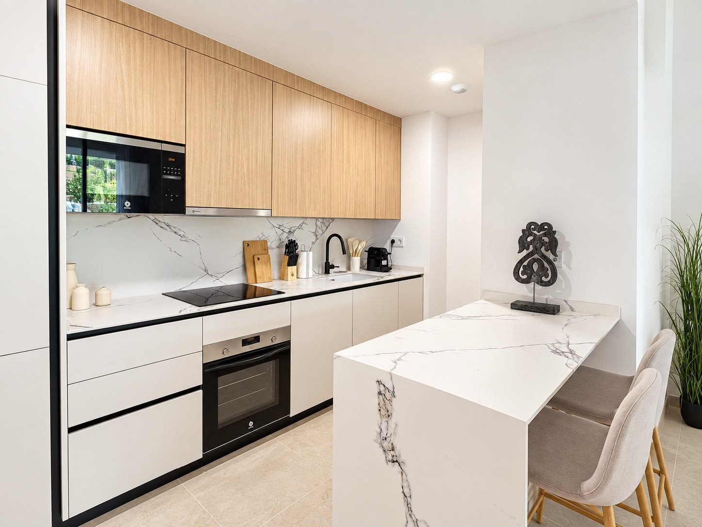 Kitchen with white marble island and countertops, light wood cabinetry, and integrated appliances.