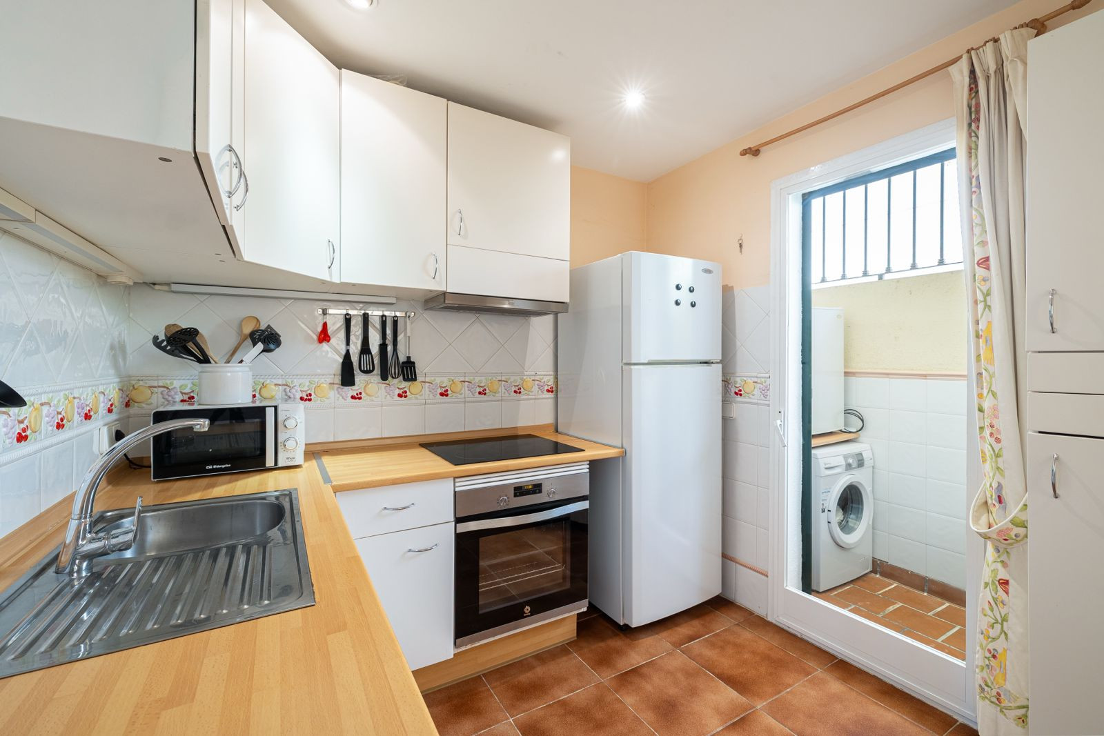 Modern kitchen with white cabinets, essential appliances, and a laundry area visible through a door.